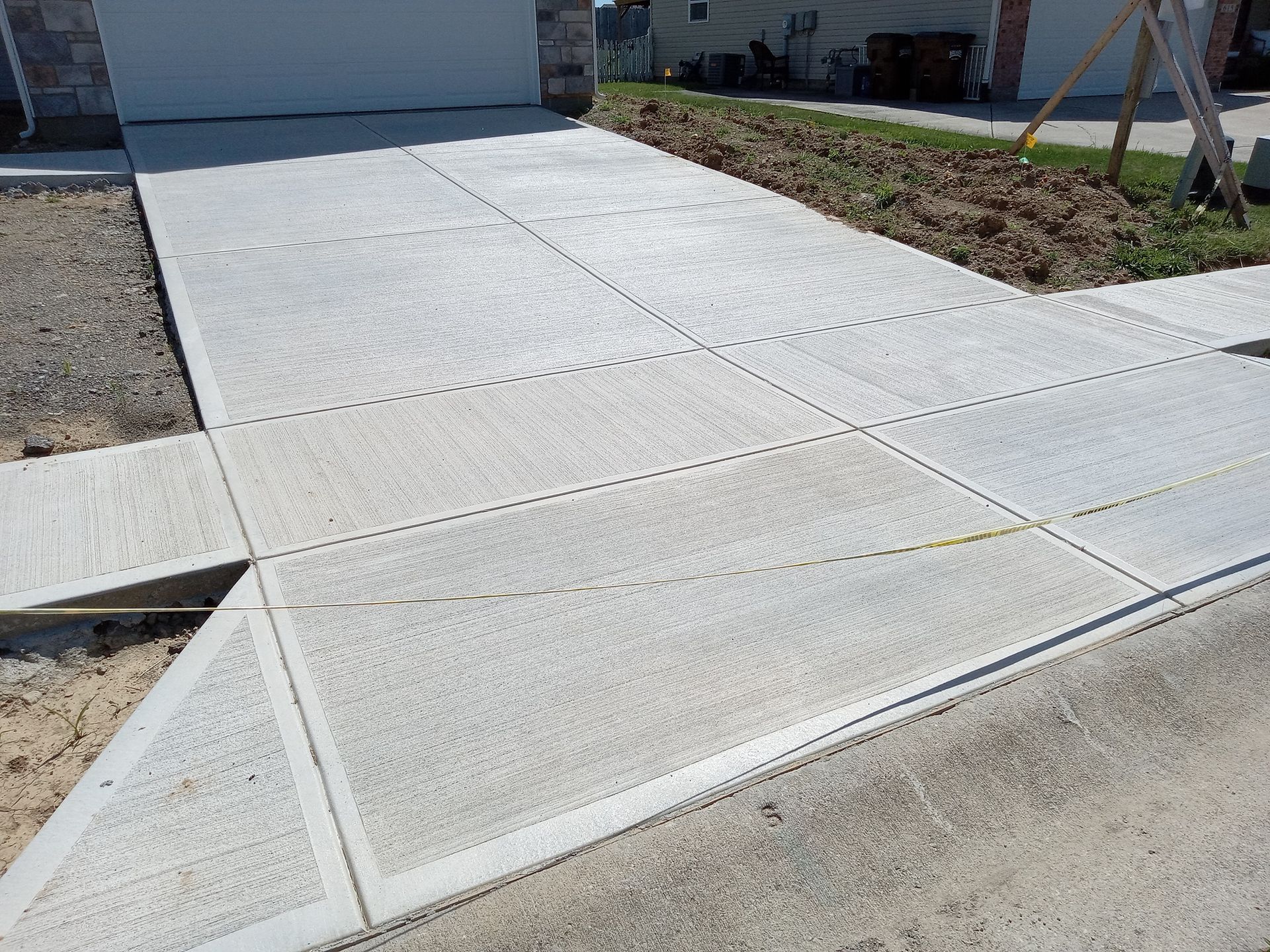 Concrete driveway with grid pattern, adjacent to a sidewalk, leading to a garage.