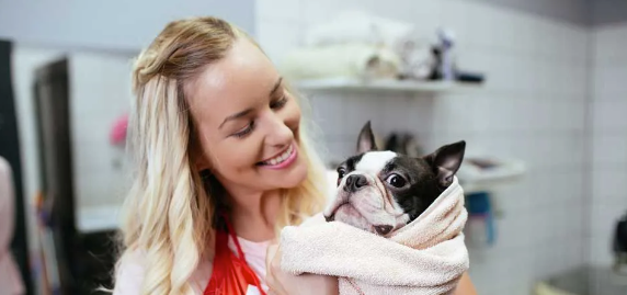 A woman is holding a small dog wrapped in a towel.