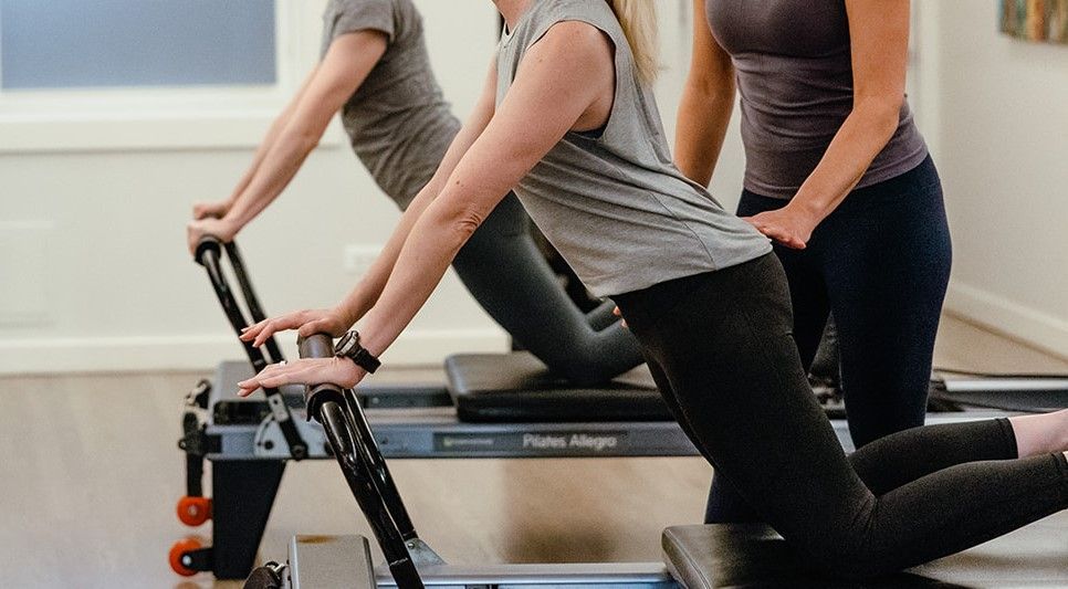 A woman is teaching another woman how to use a pilates reformer.