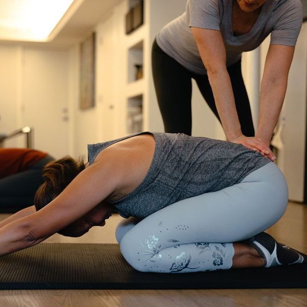 A woman is helping another woman stretch her legs on a yoga mat