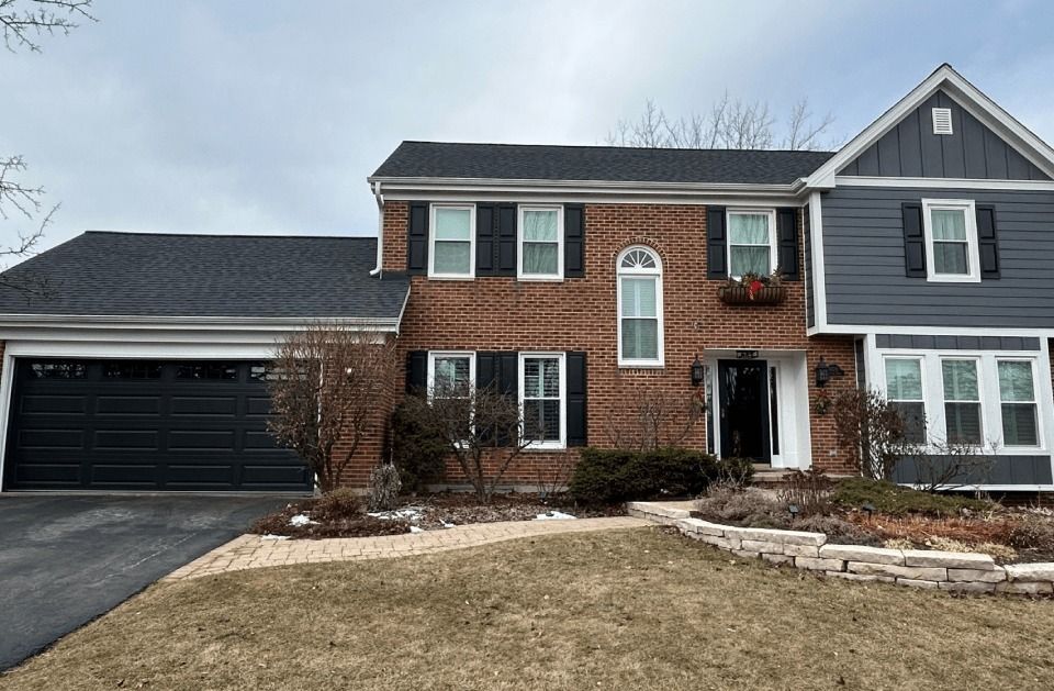 A large brick house with a black garage door and black shutters.