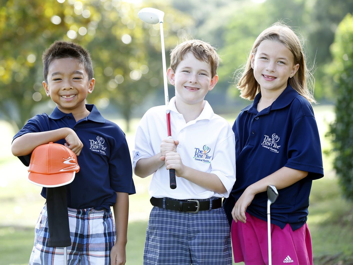A boy and two girls holding golf clubs on a golf course