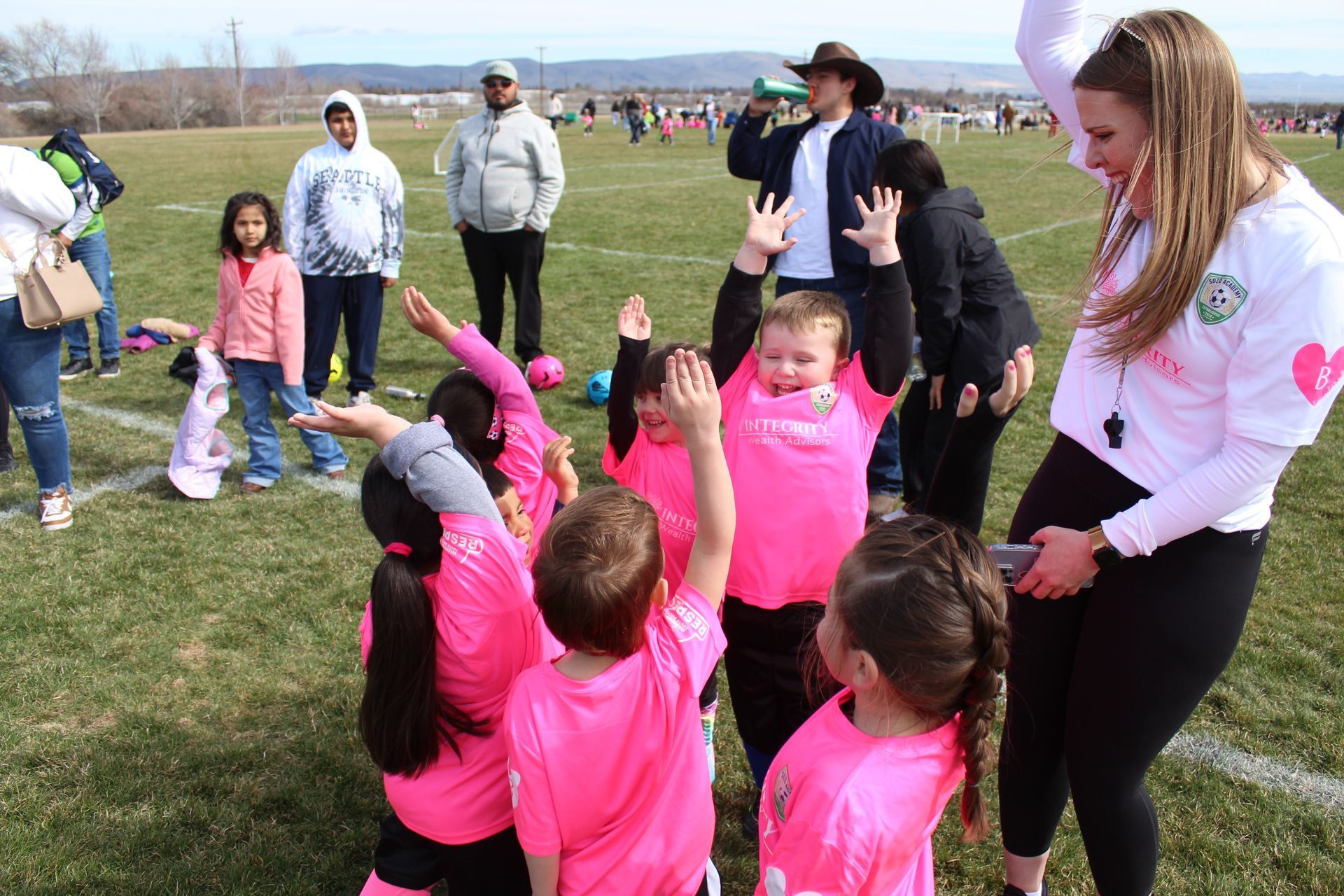 A group of children wearing pink shirts are playing on a field.
