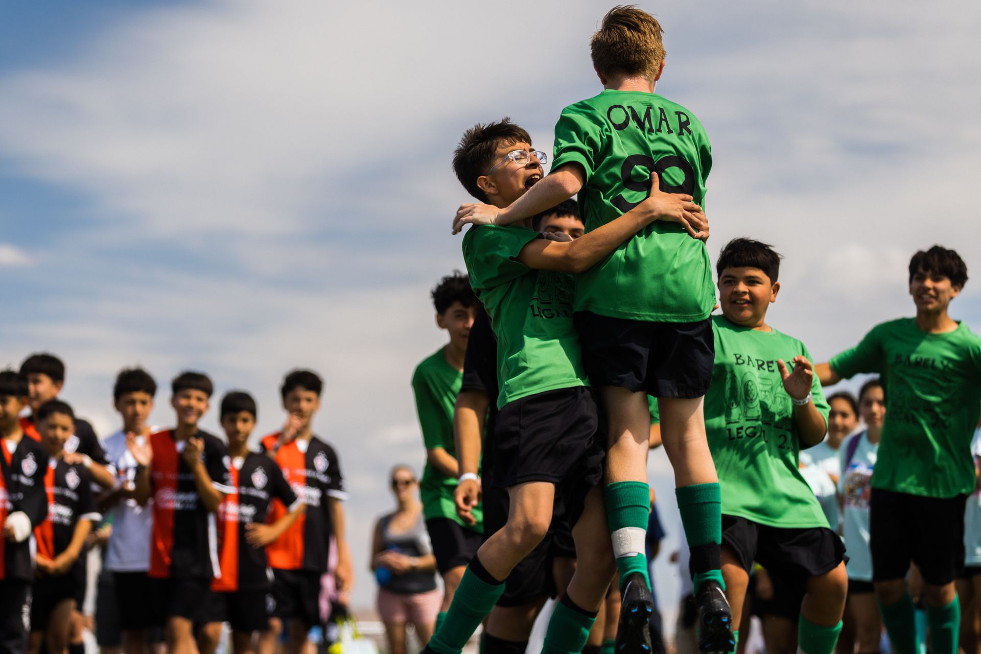 A group of young boys are hugging each other on a soccer field.