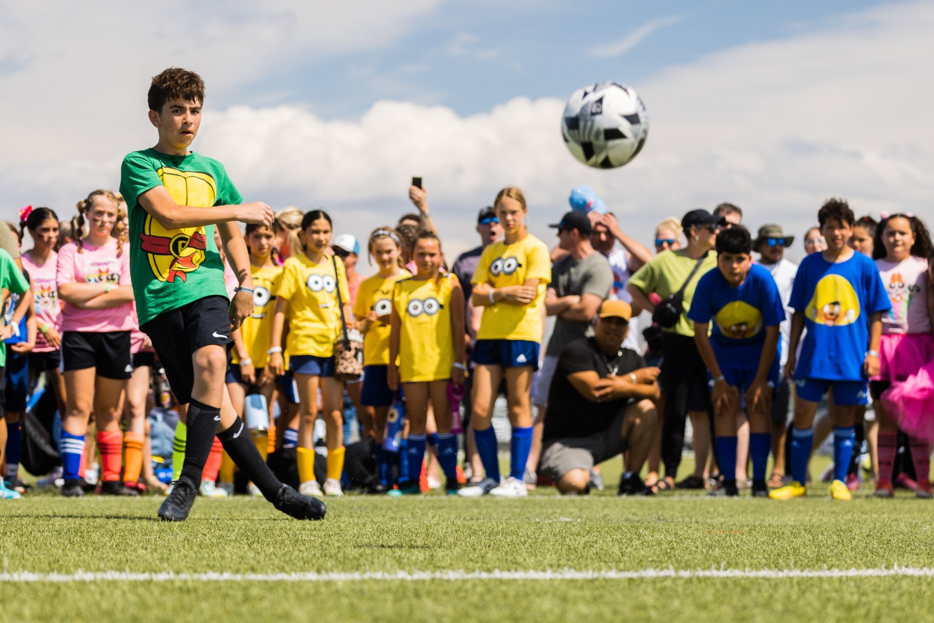 A boy is kicking a soccer ball in the air while a group of children watch.