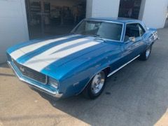 A blue and white chevrolet camaro is parked in front of a garage.