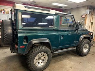 A green land rover defender is parked in a garage.