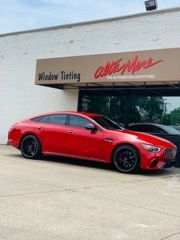 A red car is parked in front of a window tinting shop.