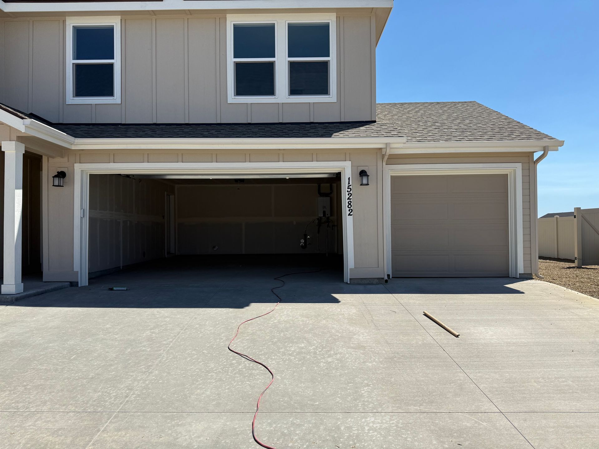 Two-story beige house with open garage and closed garage door. Concrete driveway with crack. Clear blue sky.