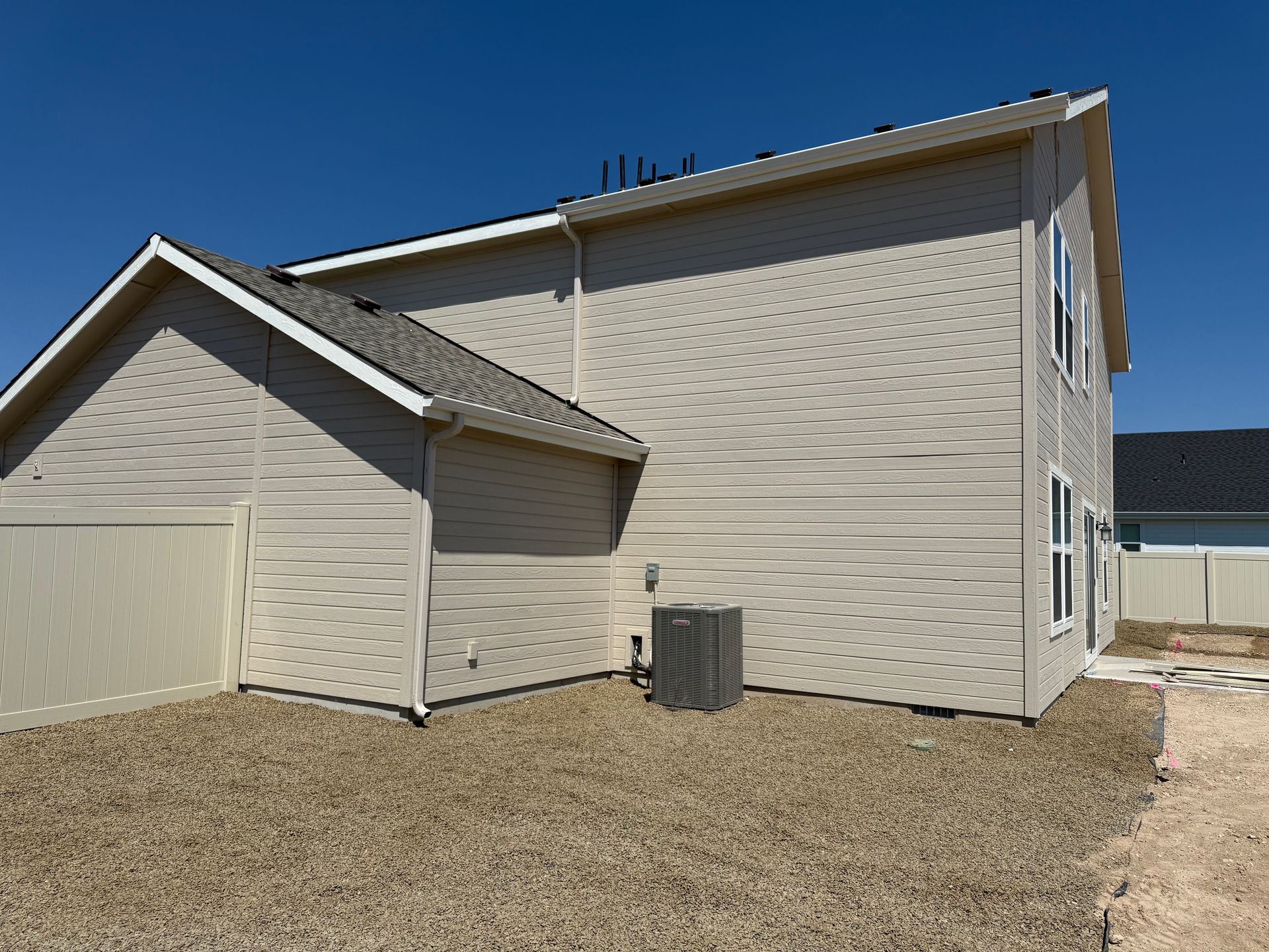 Tan house with light-colored siding, a dark roof, and an air conditioning unit. Clear blue sky.