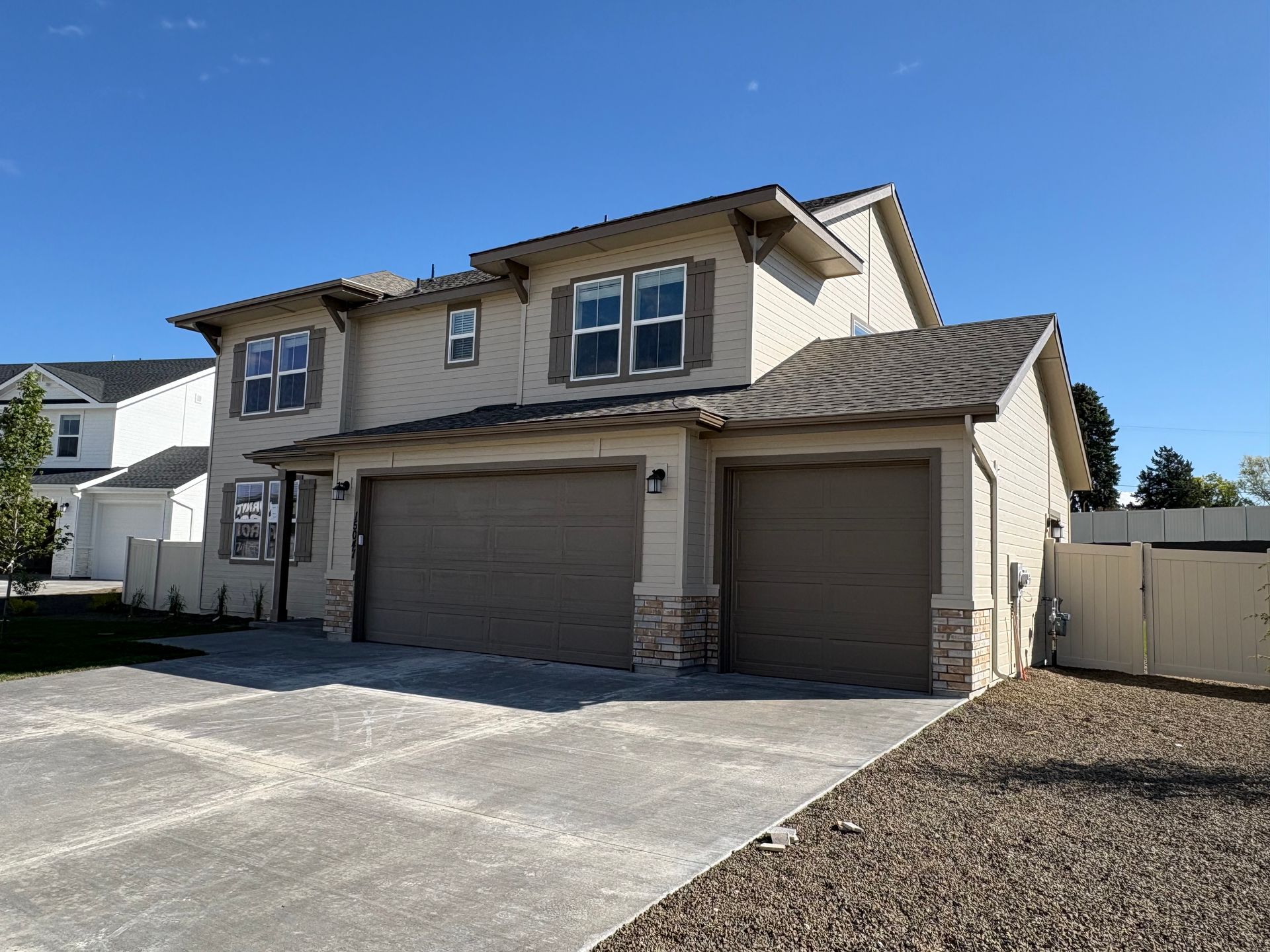 Two-story beige house with brown garage doors and a paved driveway under a blue sky.