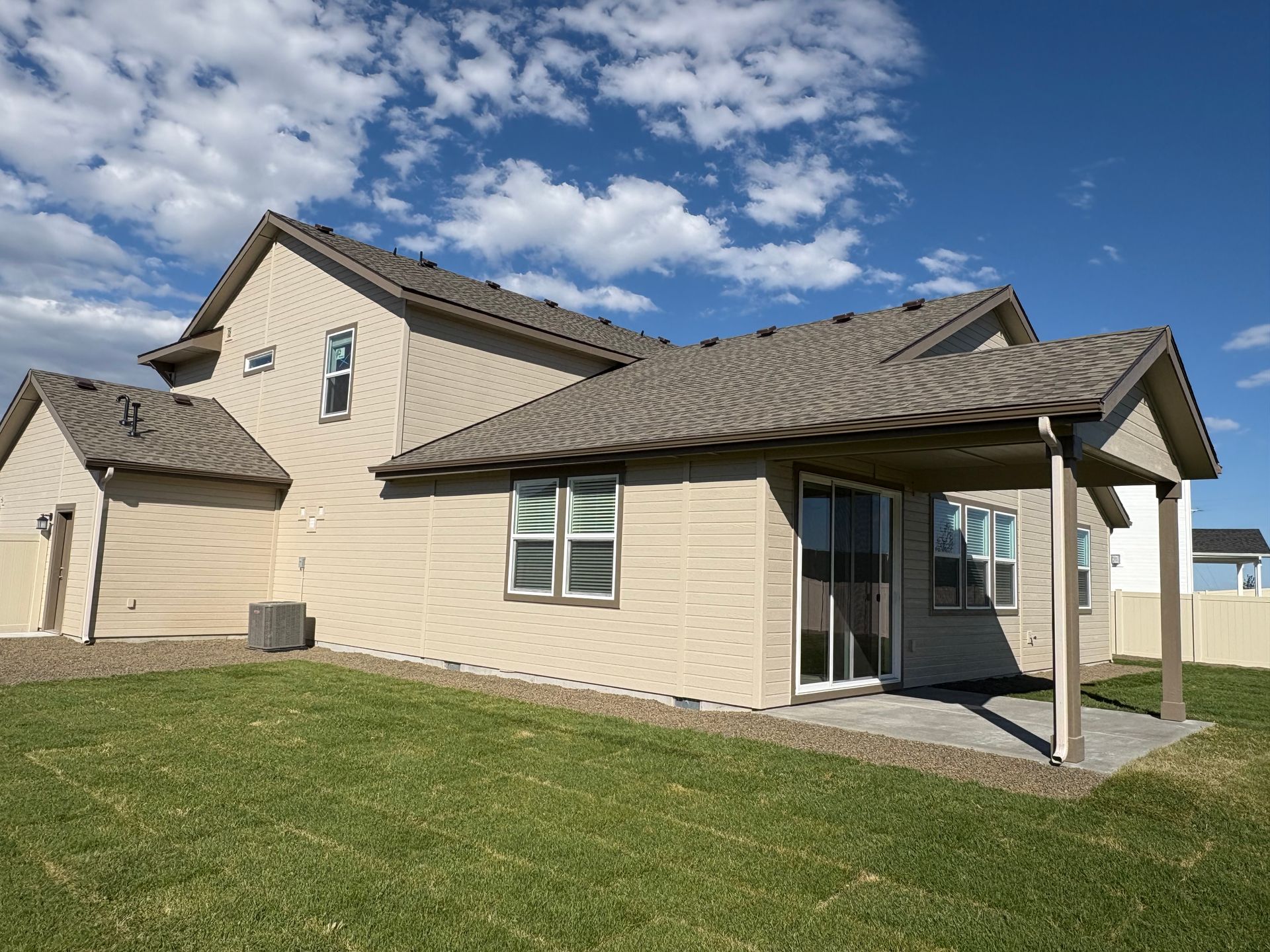 Beige house with patio and green lawn against a blue sky.