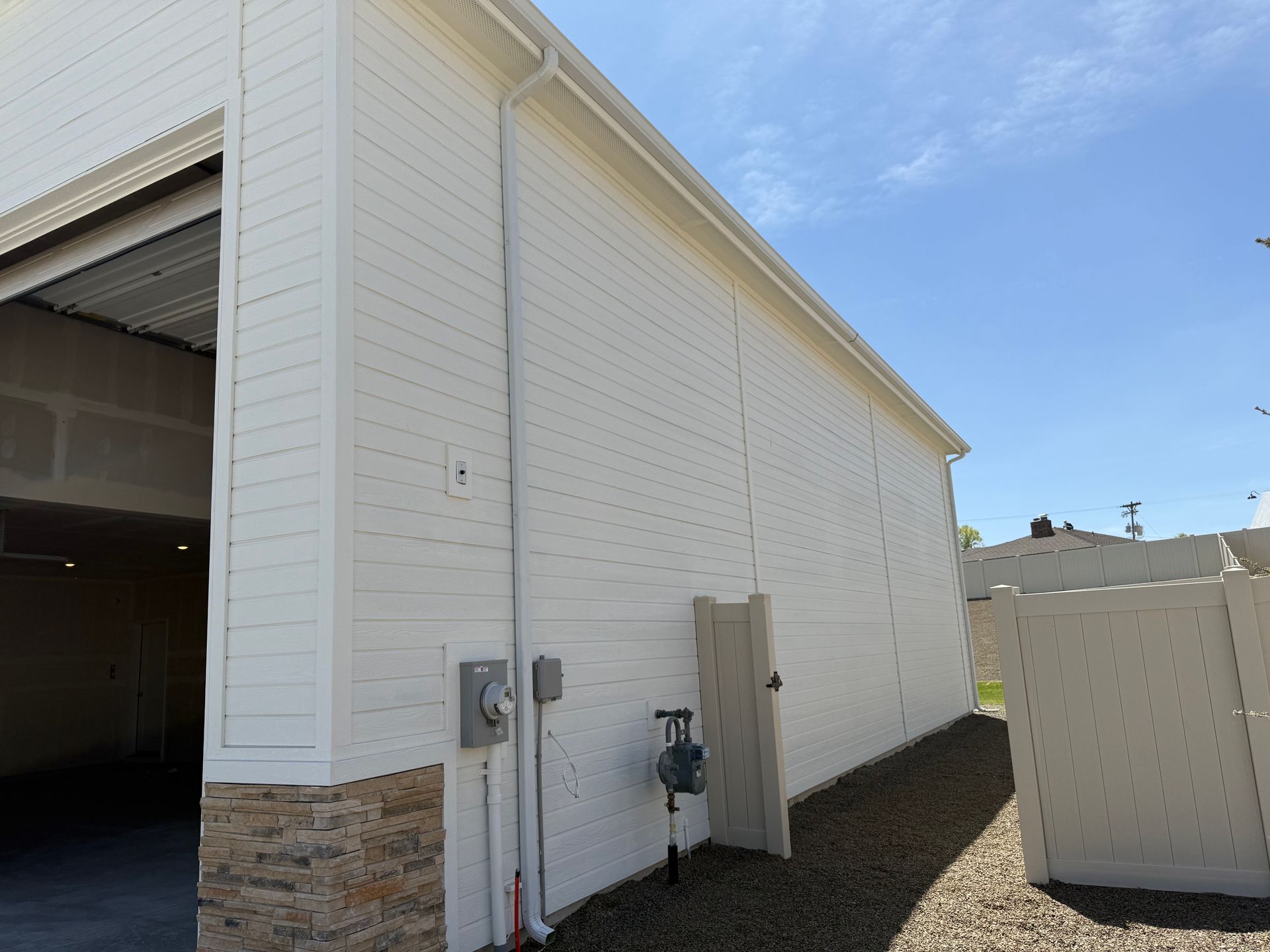 White building exterior with a garage door open and gutters, next to a gravel area.