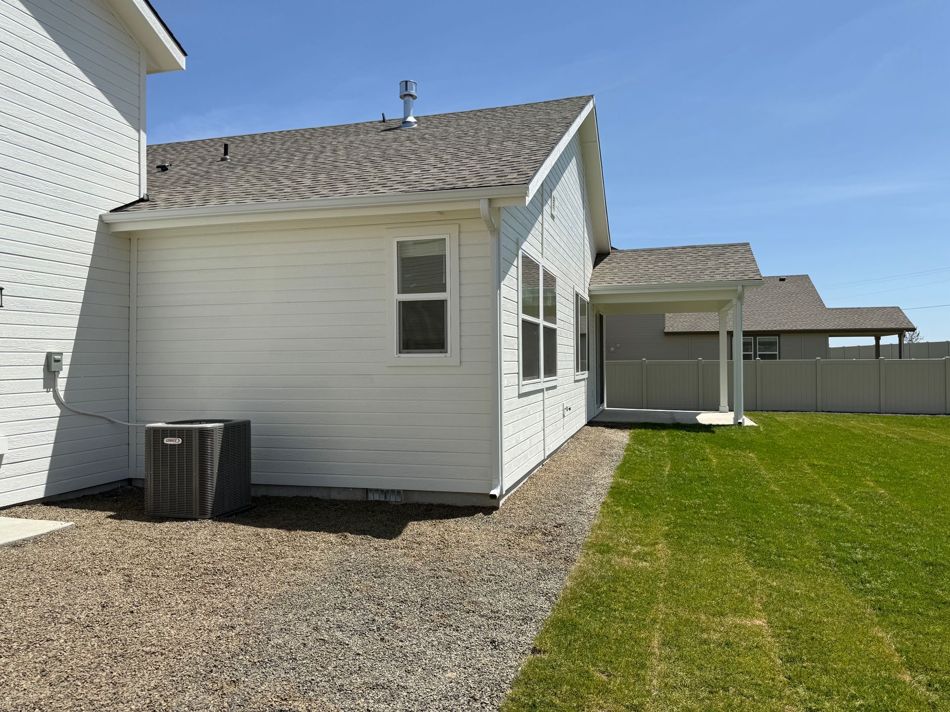 Side view of a white house with a gravel bed, air conditioning unit, and a small patch of grass.
