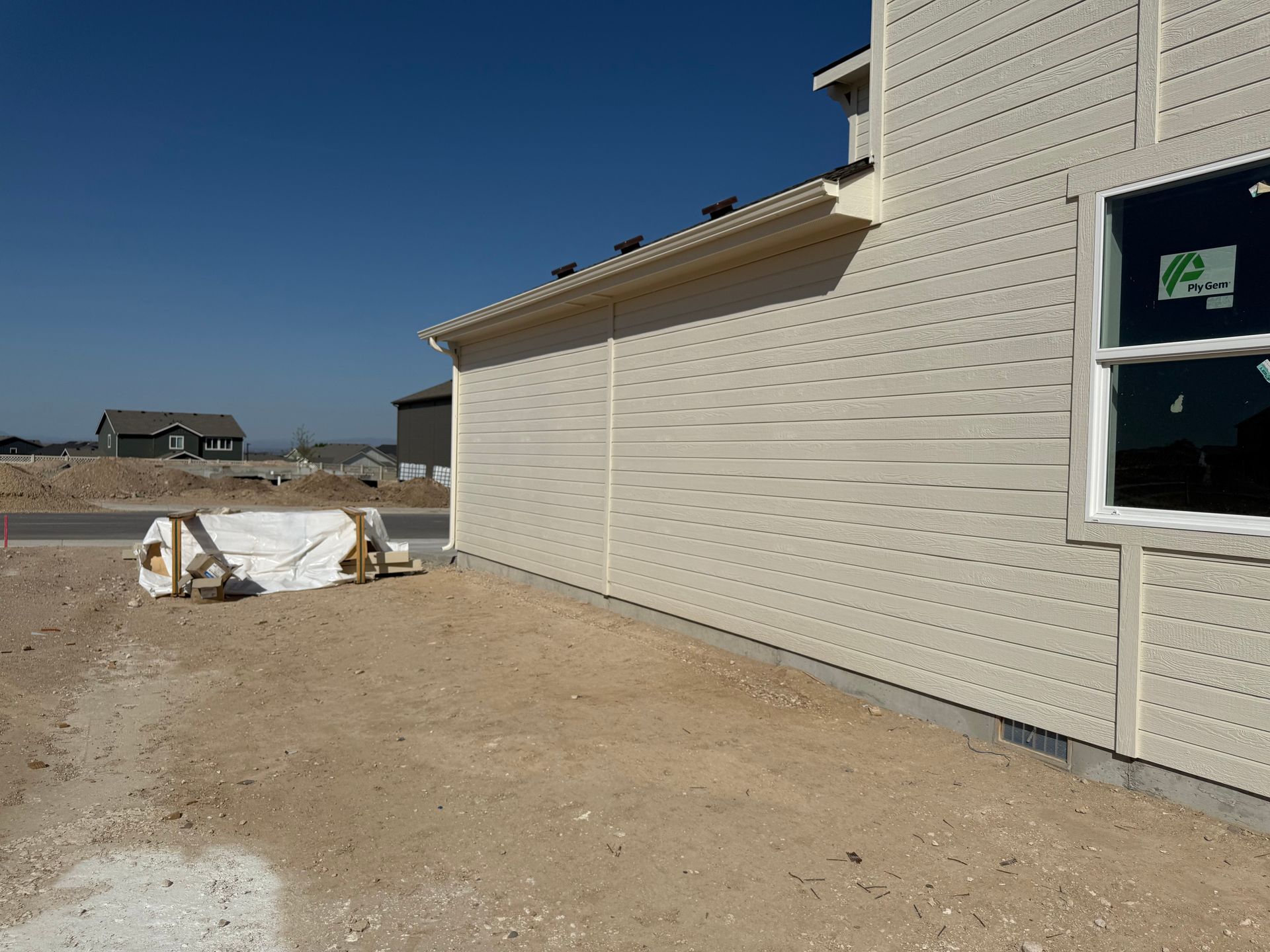 Side view of a house under construction with tan siding, blue sky, and gravel lot.
