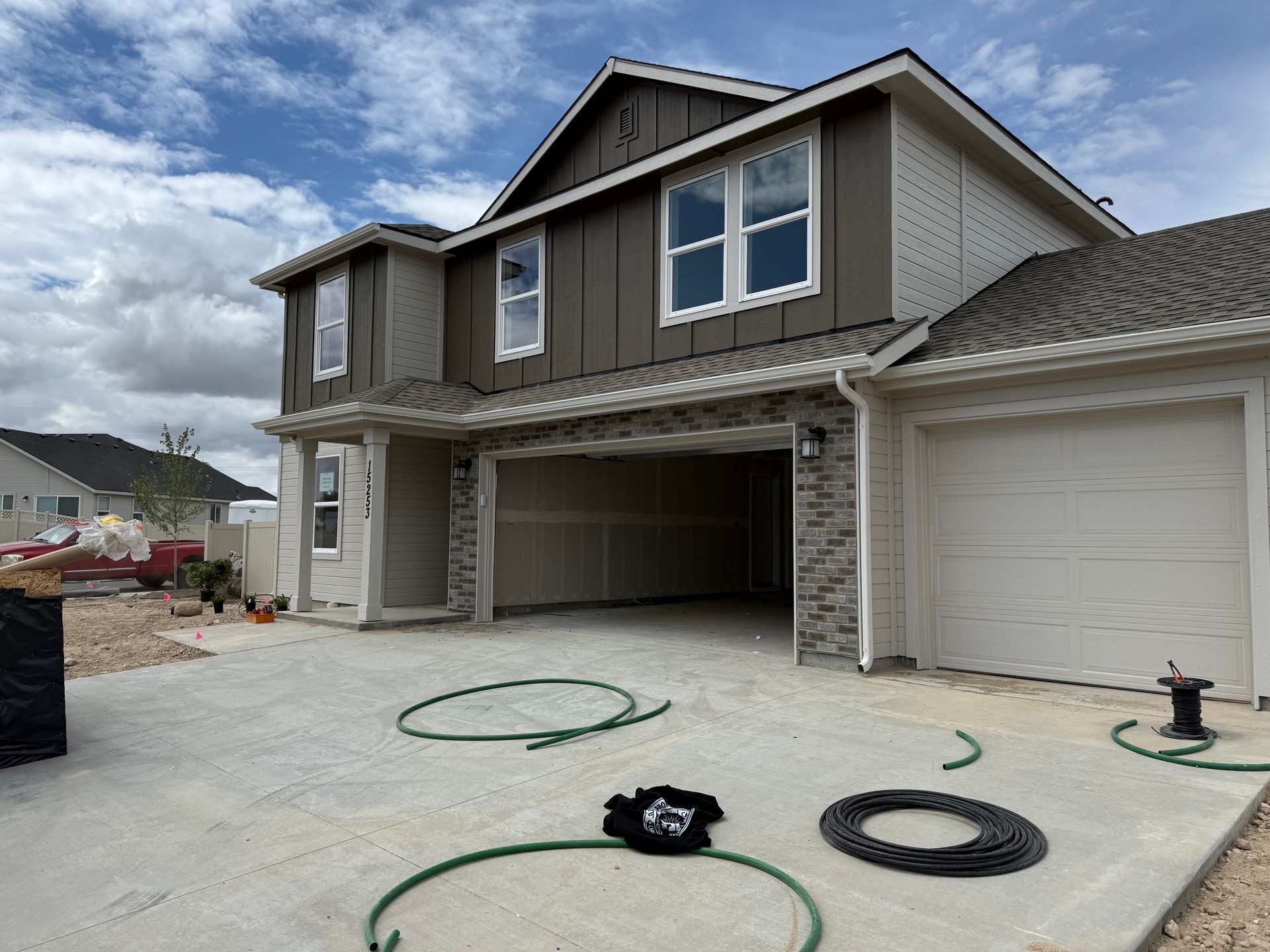 Two-story house with open garage doors and concrete driveway; tan and brown exterior, cloudy sky.