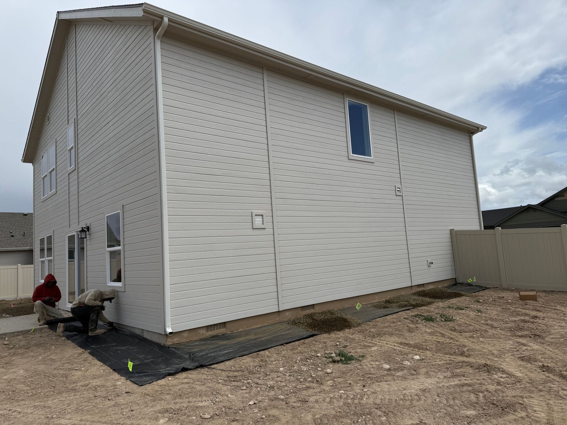Two-story house exterior with workers; beige siding, white trim, cloudy sky.