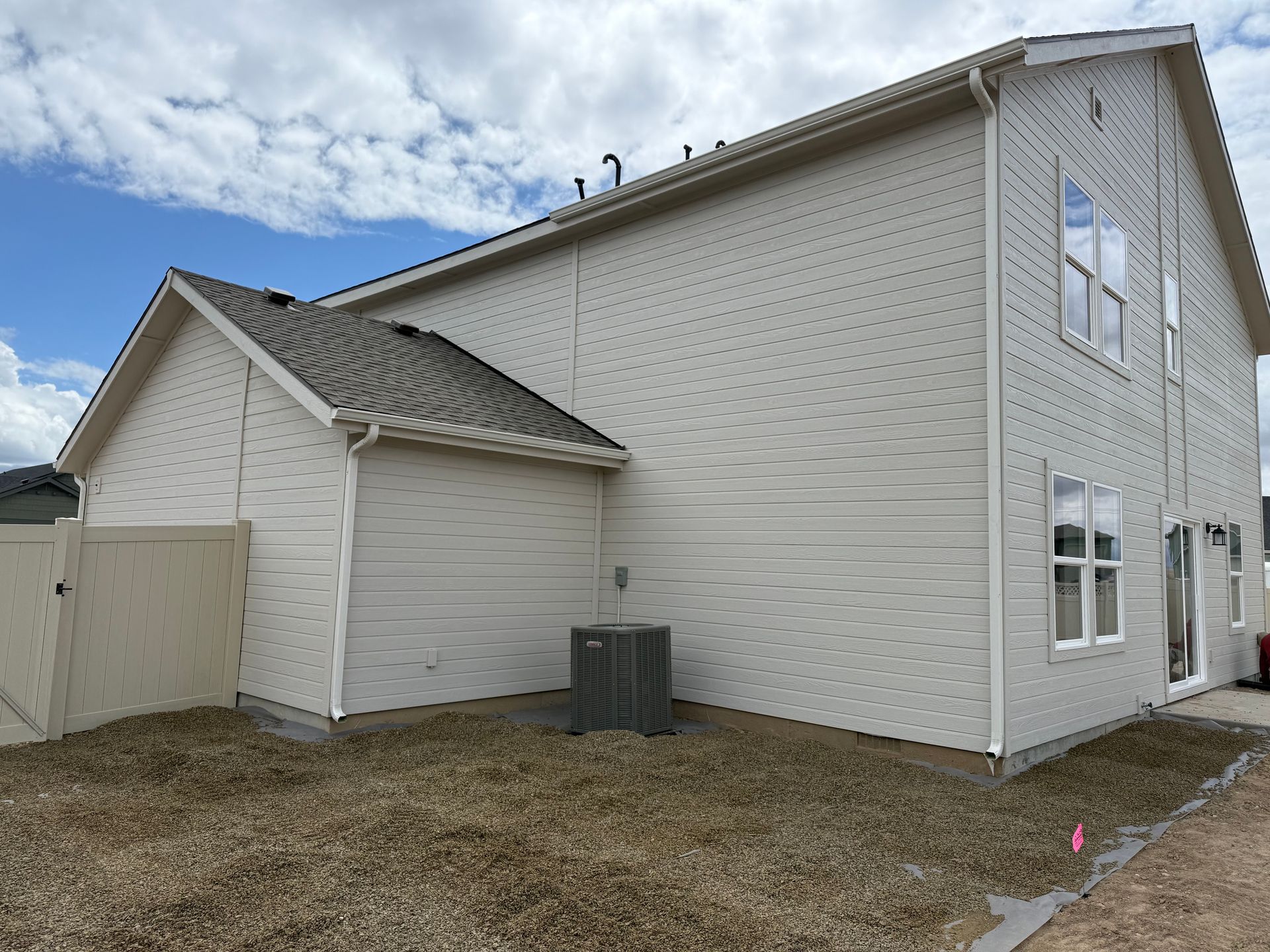 Two-story beige house with an attached single-story section, set against a cloudy sky.