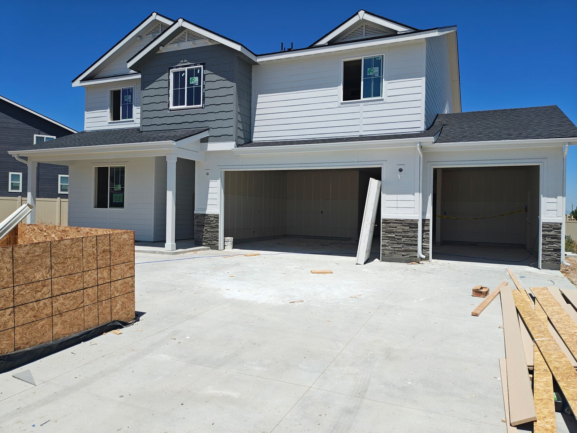 New two-story house under construction with a two-car garage, gray siding, and a concrete driveway.