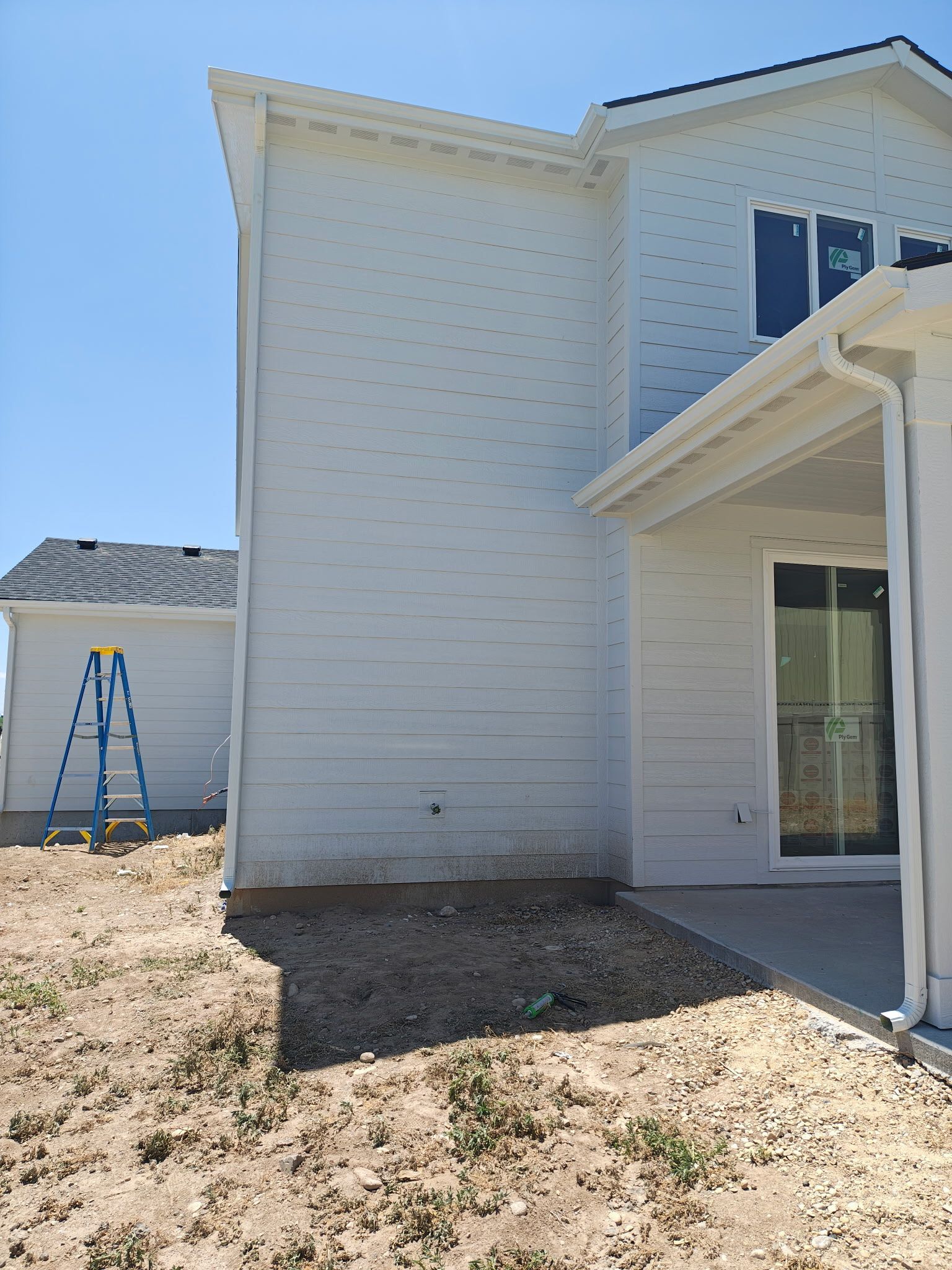 Exterior view of a new white house with siding and a patio. A blue ladder is in the background.