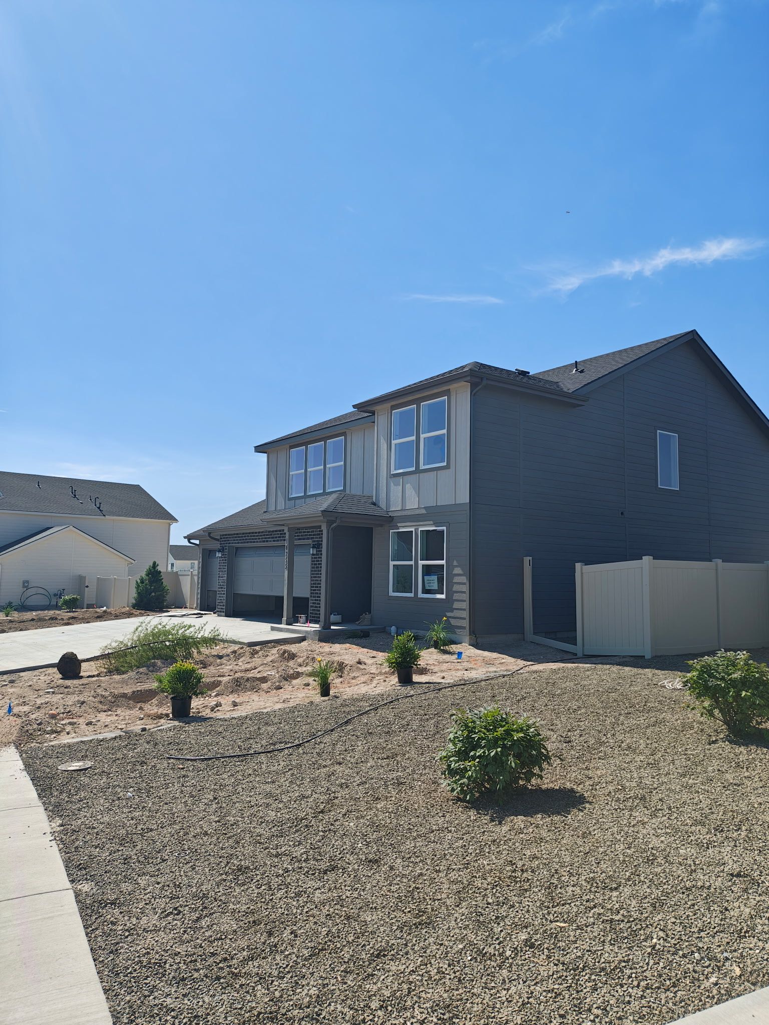 Two-story house with gray exterior and gravel yard under a blue sky.