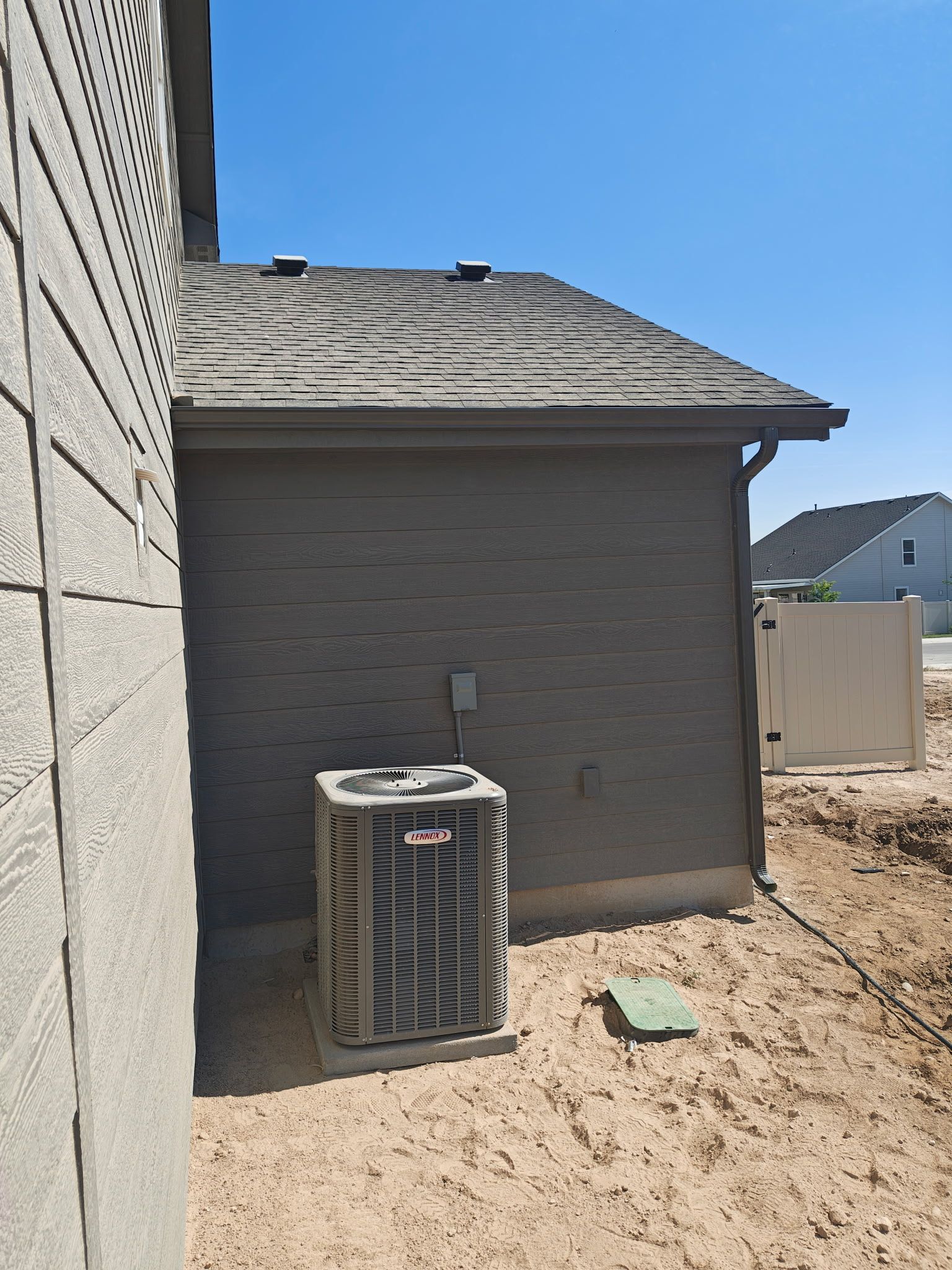 Air conditioning unit outside a building, set on a gravel area with the roof visible on a sunny day.