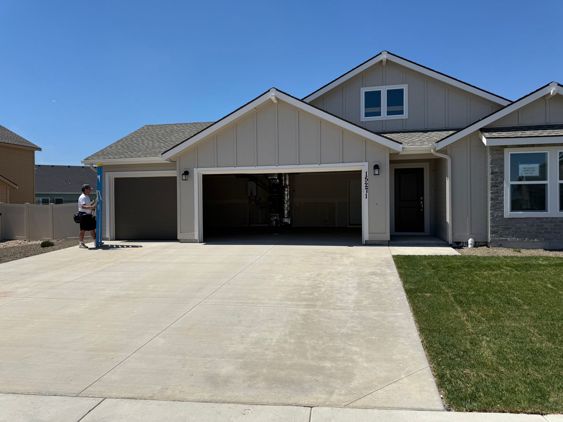 Beige house with open garage doors and a concrete driveway on a sunny day. A person stands nearby.
