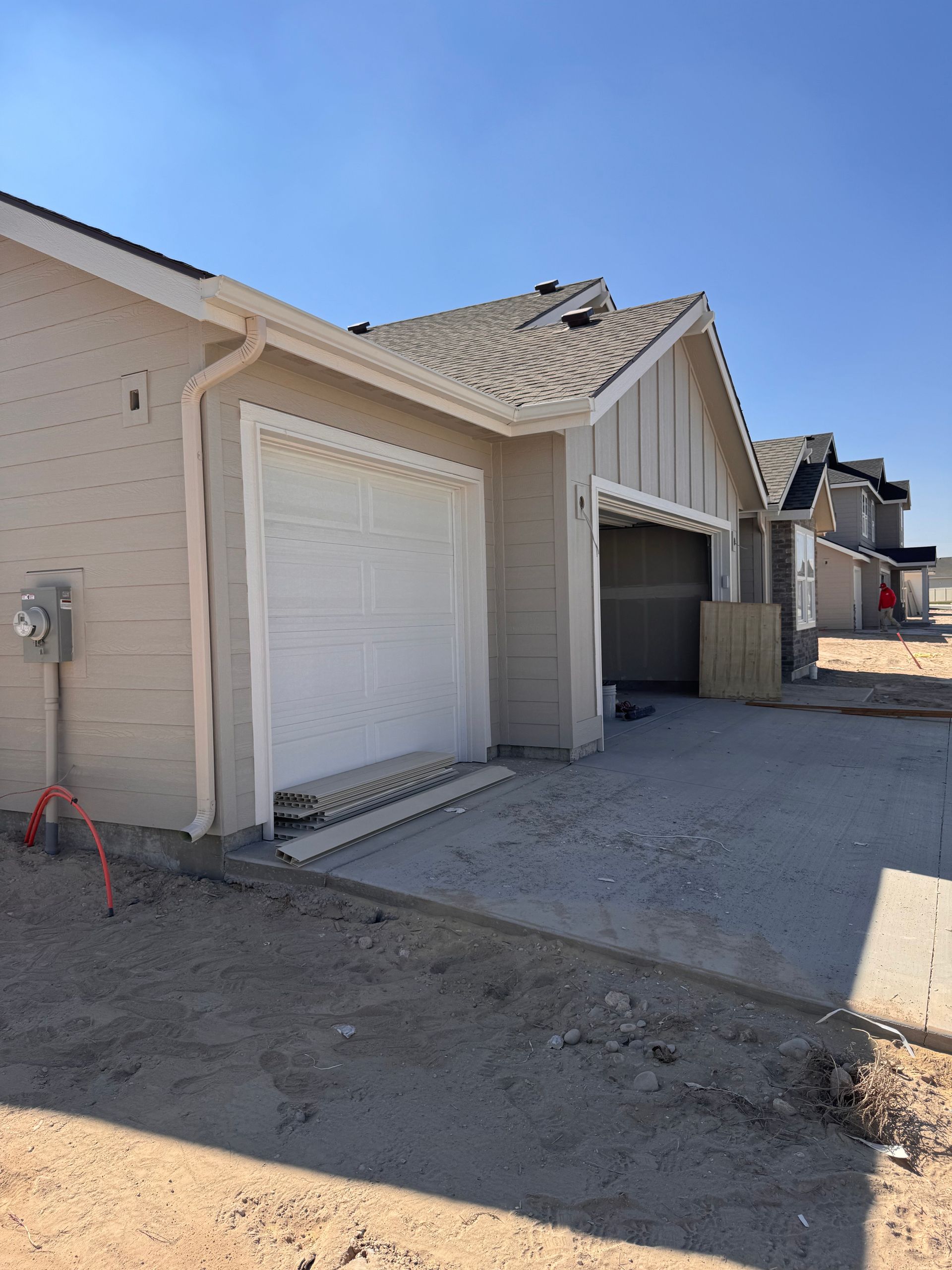 Newly constructed beige townhouses with open and closed garage doors and gravel driveways under a clear blue sky.