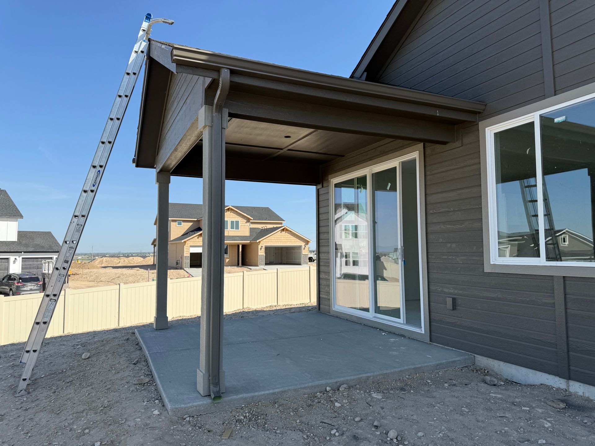 A partially built house exterior with a patio and ladder. The house is gray with a blue sky background.