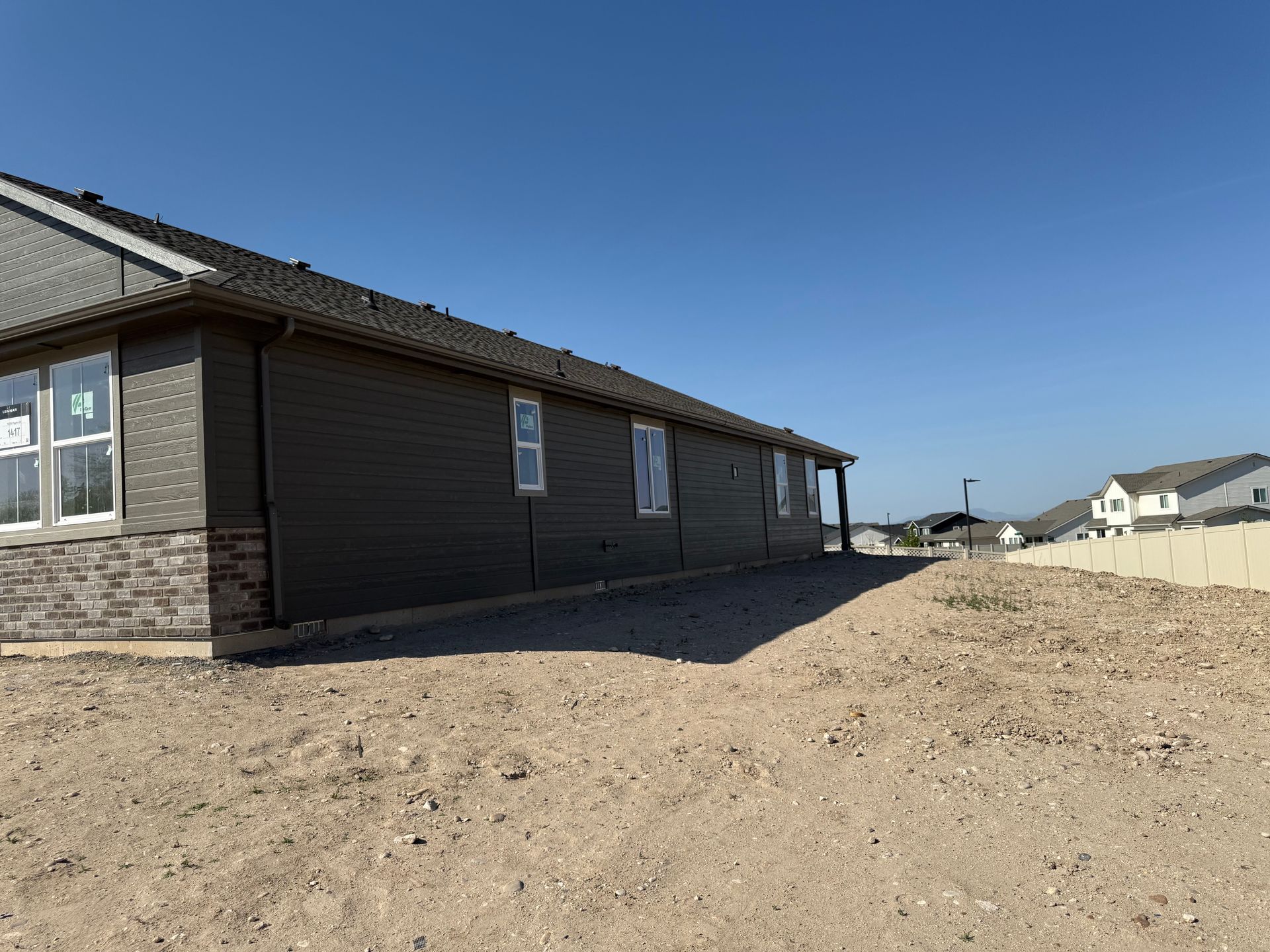 Side view of a new house under construction; dark gray siding, windows, and a gravel yard against a blue sky.