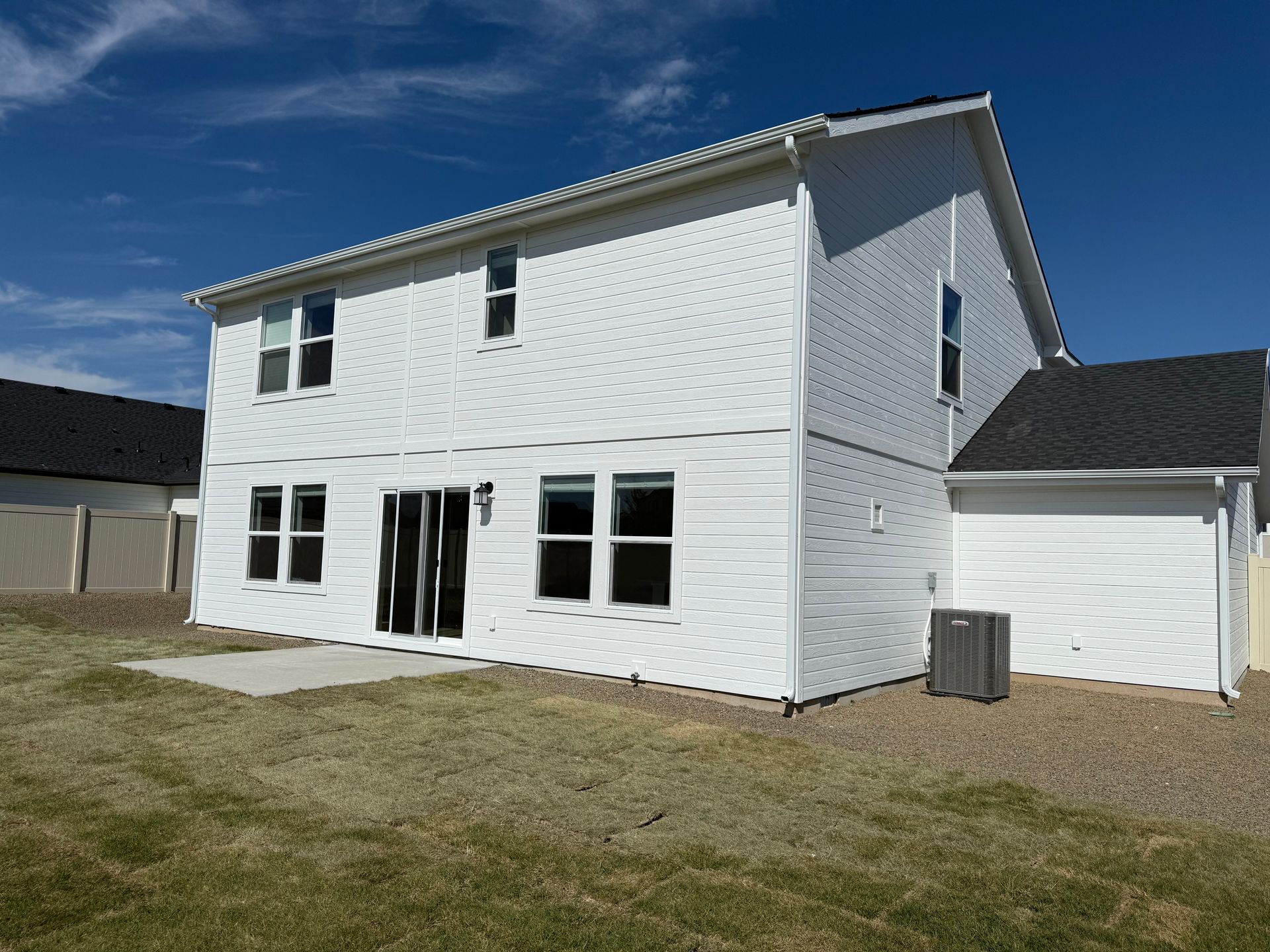Back of a white two-story house with black roof, windows, and sliding glass door. A/C unit on side. Blue sky.