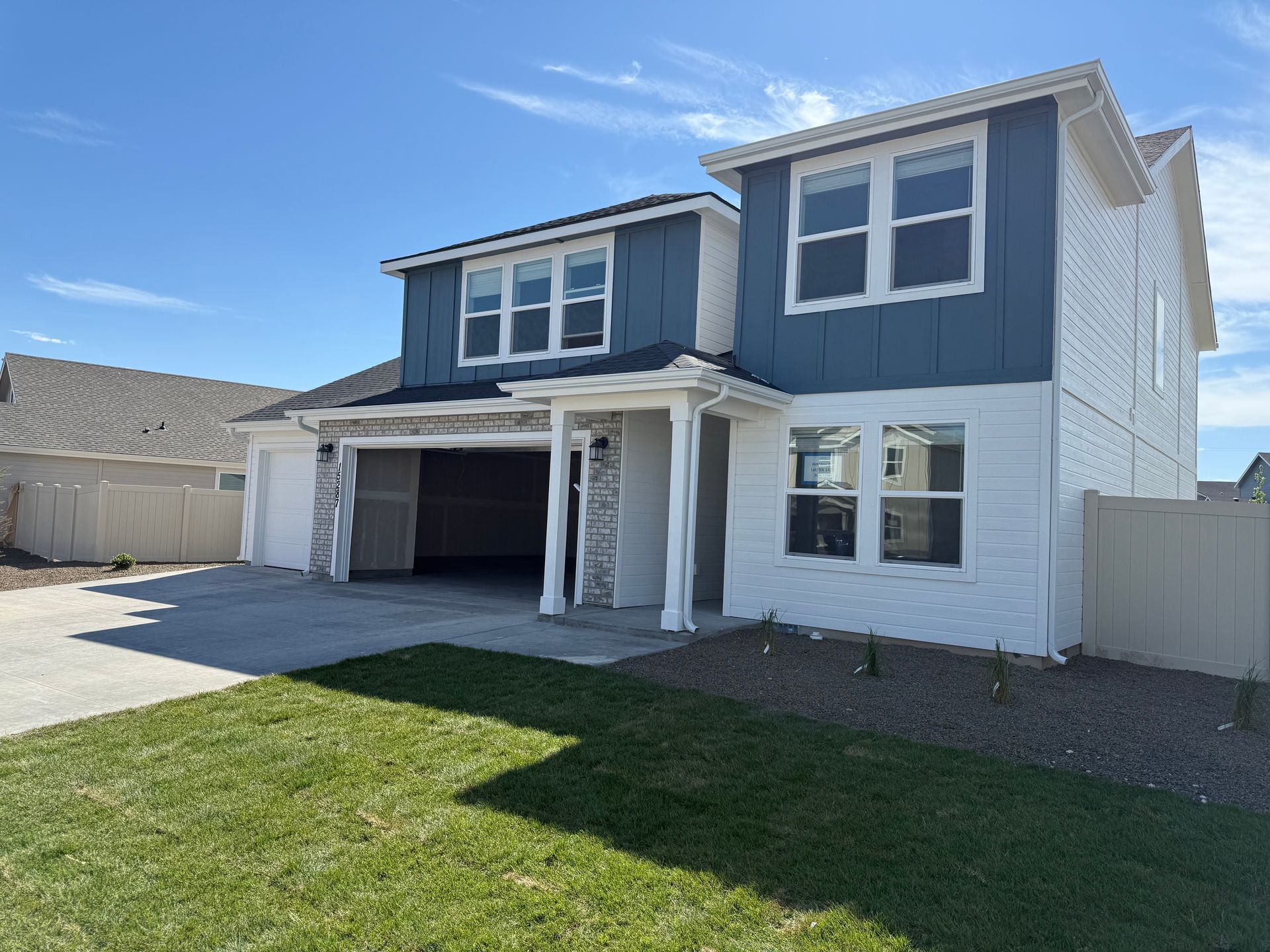Two-story house with blue siding, white trim, and a two-car garage under a blue sky.
