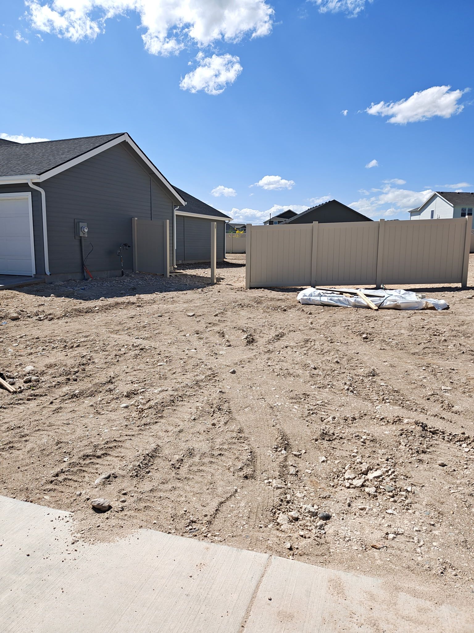 A dirt lot with tire tracks, houses, and a fence under a blue sky.
