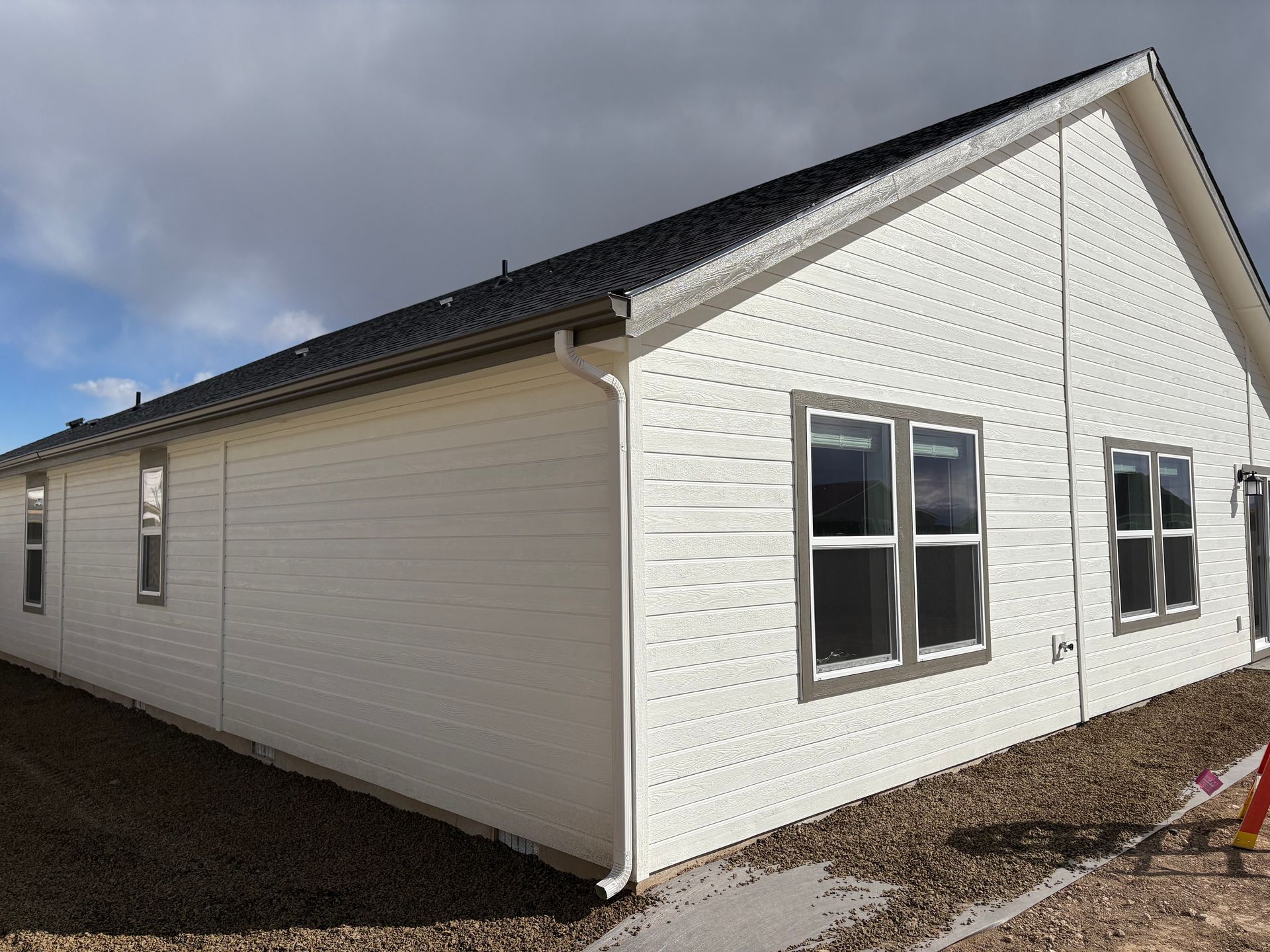 White house with black roof, windows, and gutters against a cloudy sky.