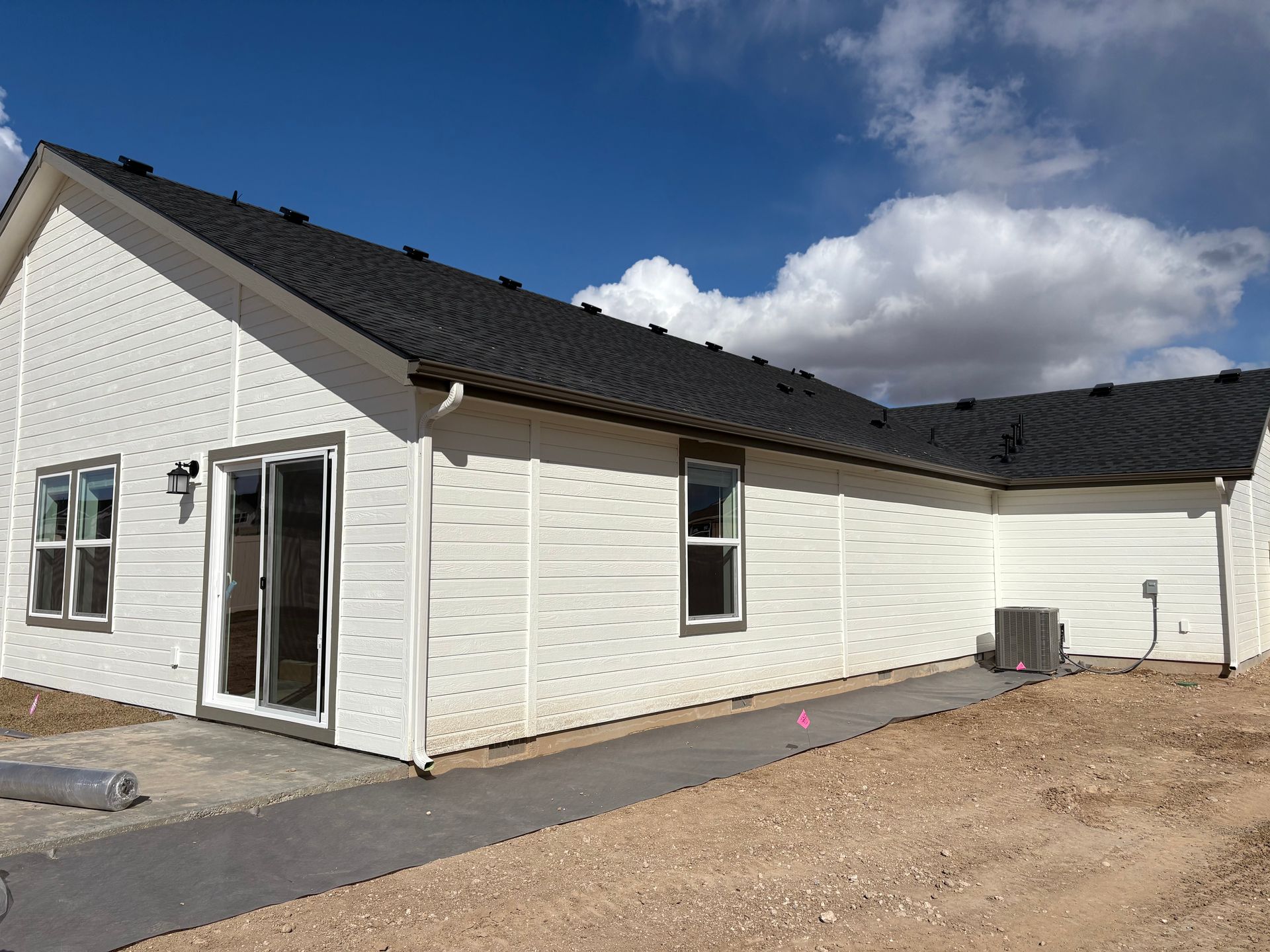 White house exterior with dark roof, windows, and sliding glass door; cloudy sky.