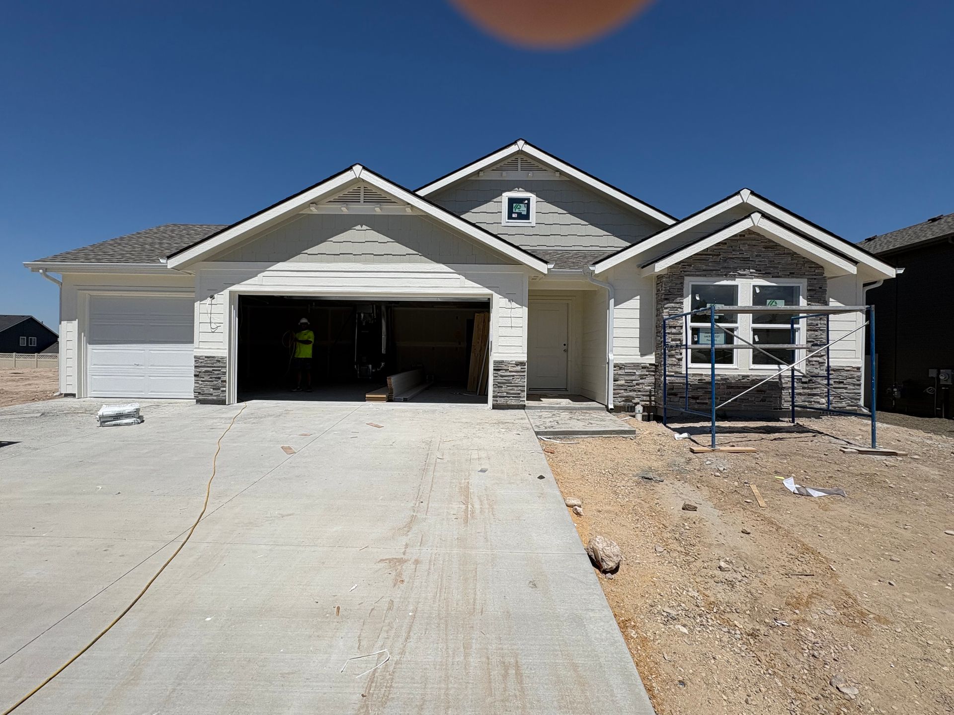 New house under construction with light gray siding, stone accents, and a concrete driveway.