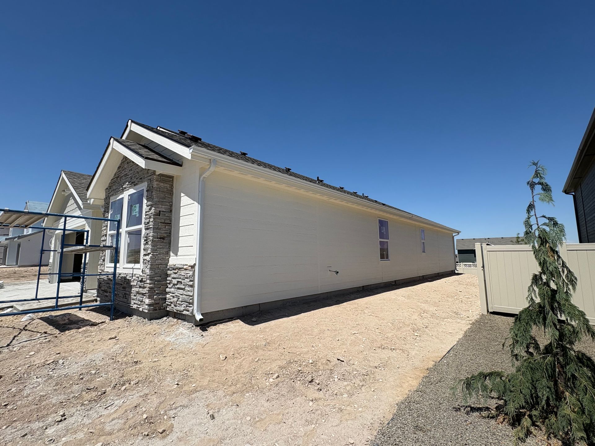 Side view of a house under construction with light siding, a stone accent wall, and gravel ground.