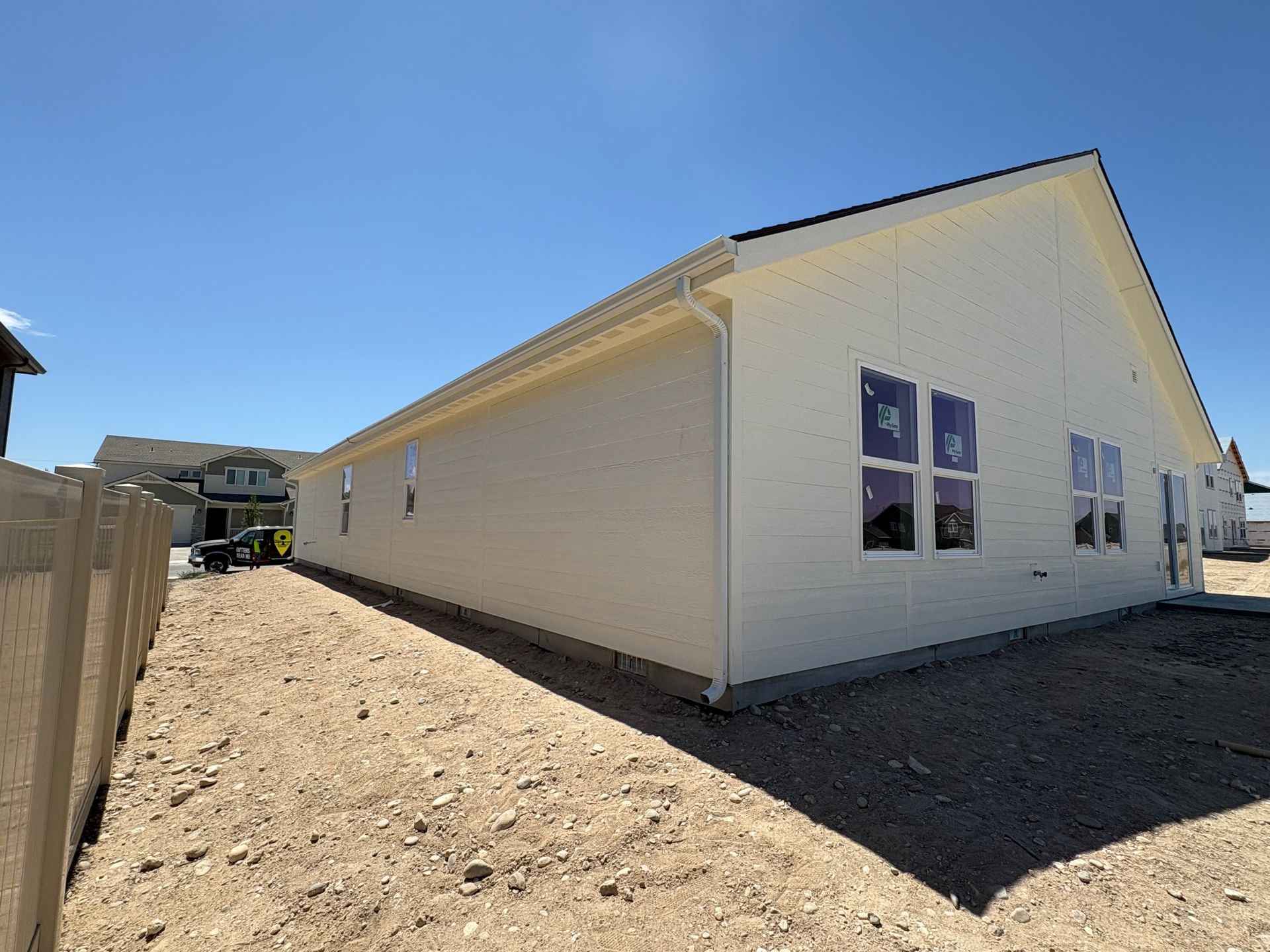 Side view of a light-colored house under construction, with windows and a fence on a sunny day.
