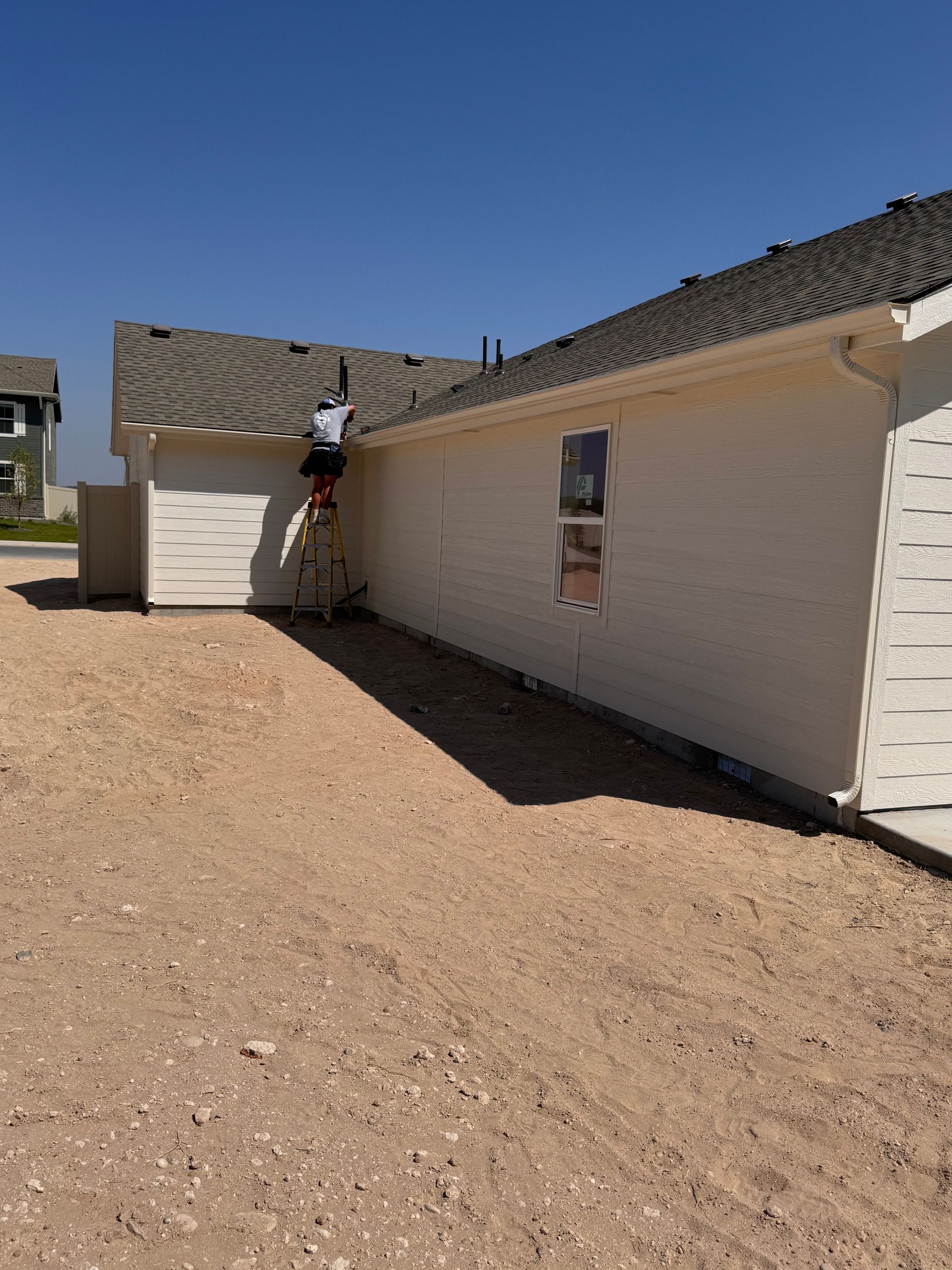 Person on a ladder working on the roof of a house under construction. Exterior view on a sunny day.