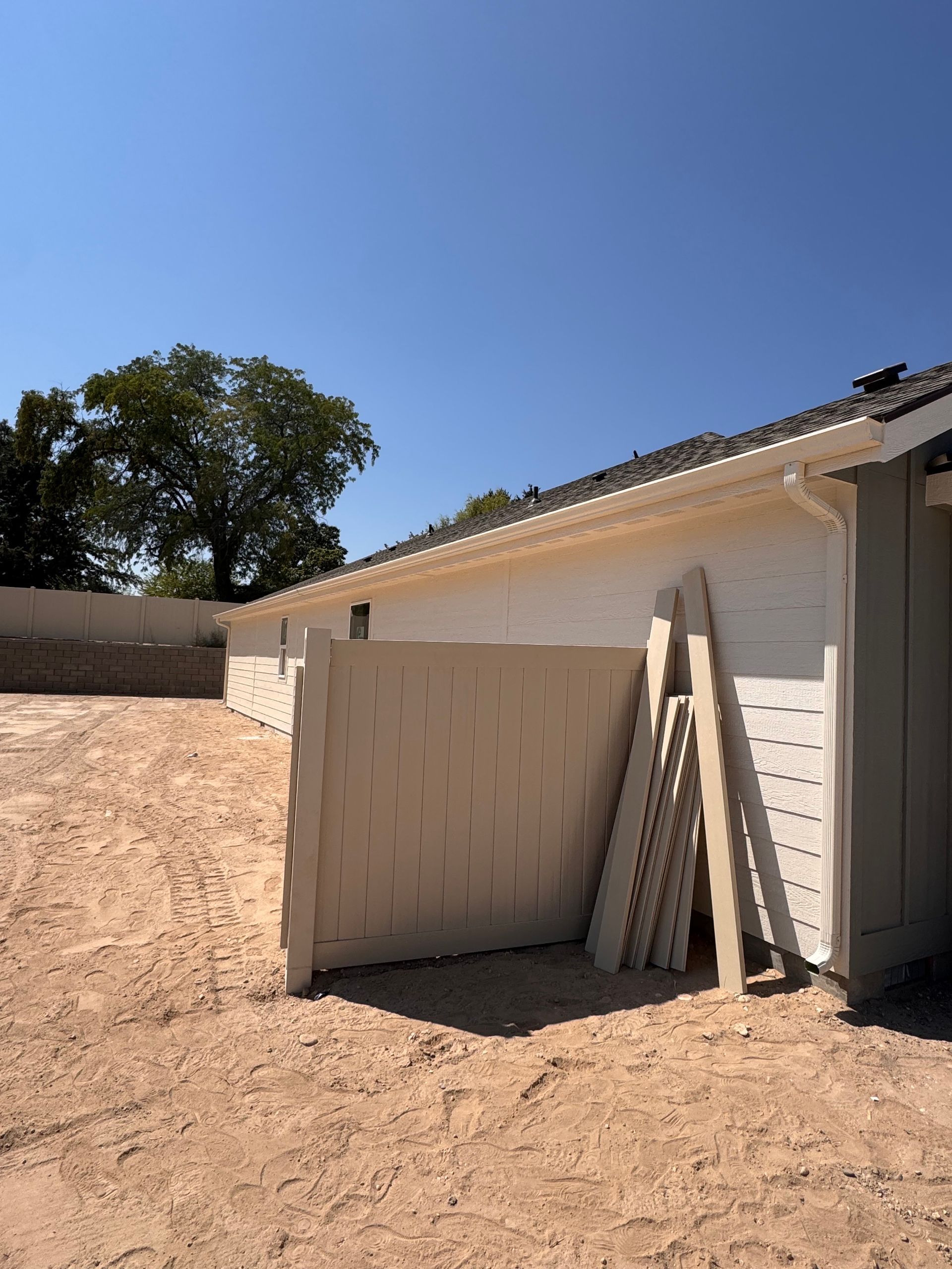 Construction site with beige fence, building, and panels. Brown dirt under blue sky.