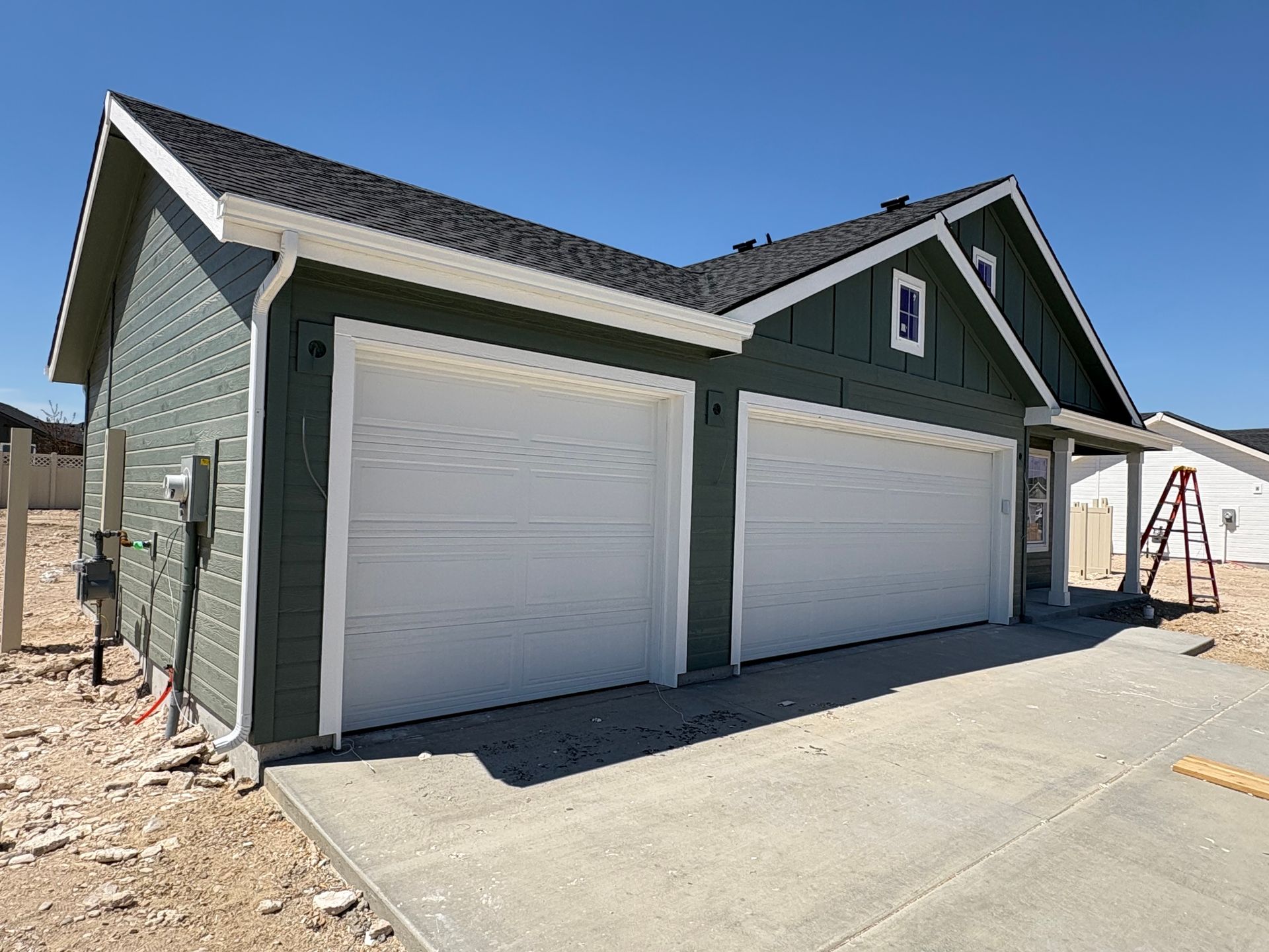 Green-sided house with white garage doors and trim, black roof, and a clear blue sky.