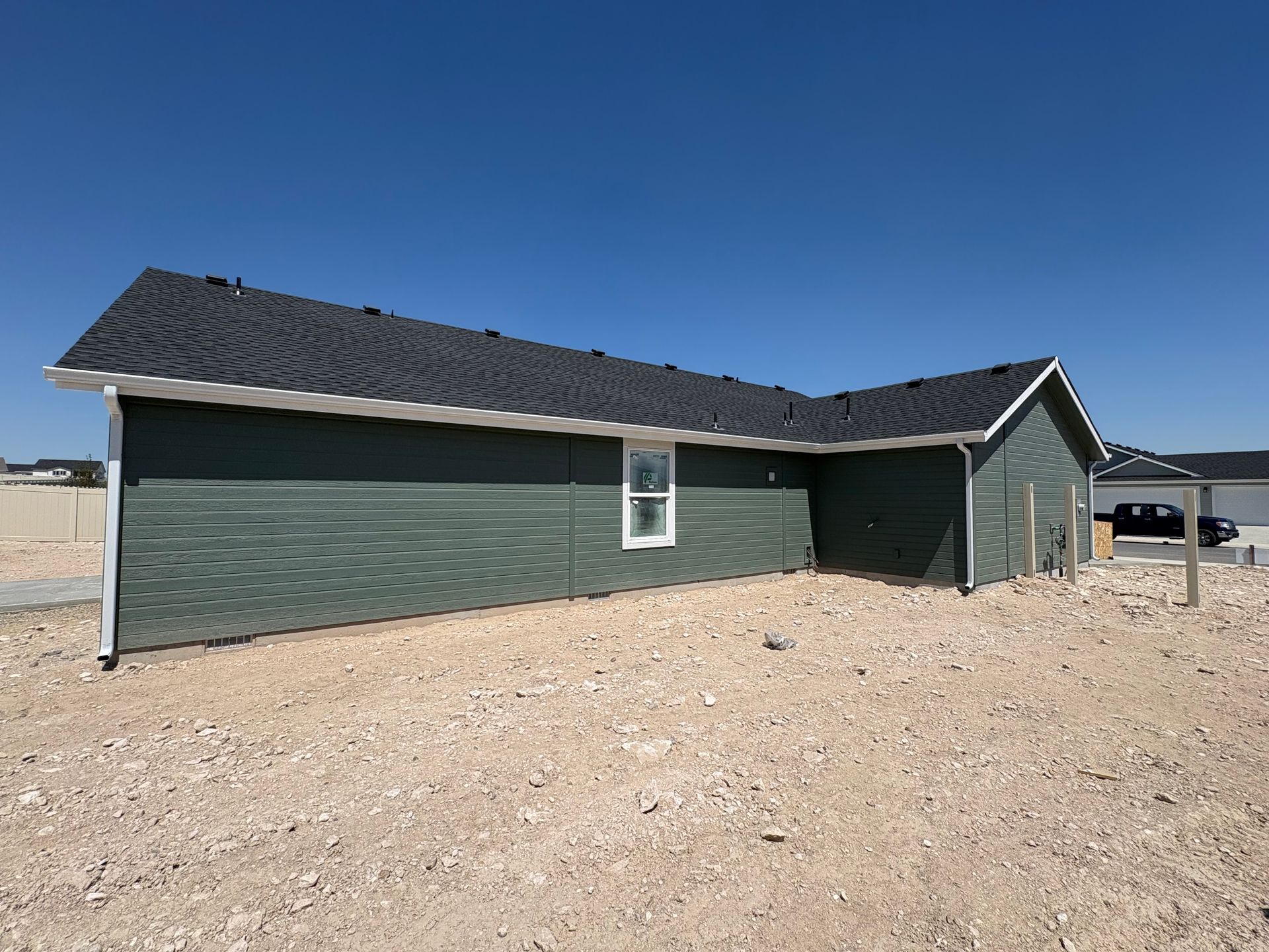 Green-sided house with a black roof and white trim under a clear blue sky.