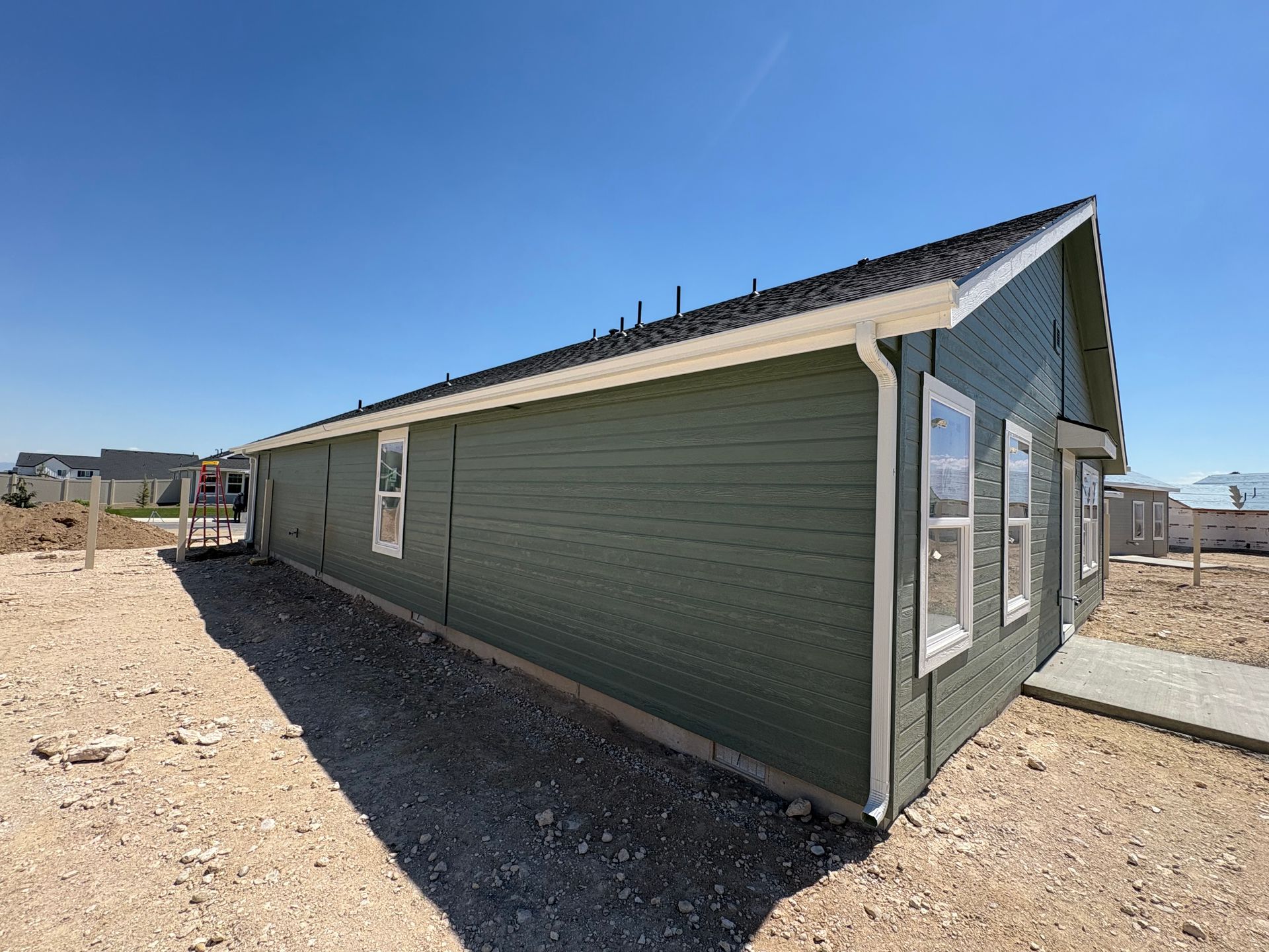 Green house under construction on a dirt lot, white trim, blue sky.