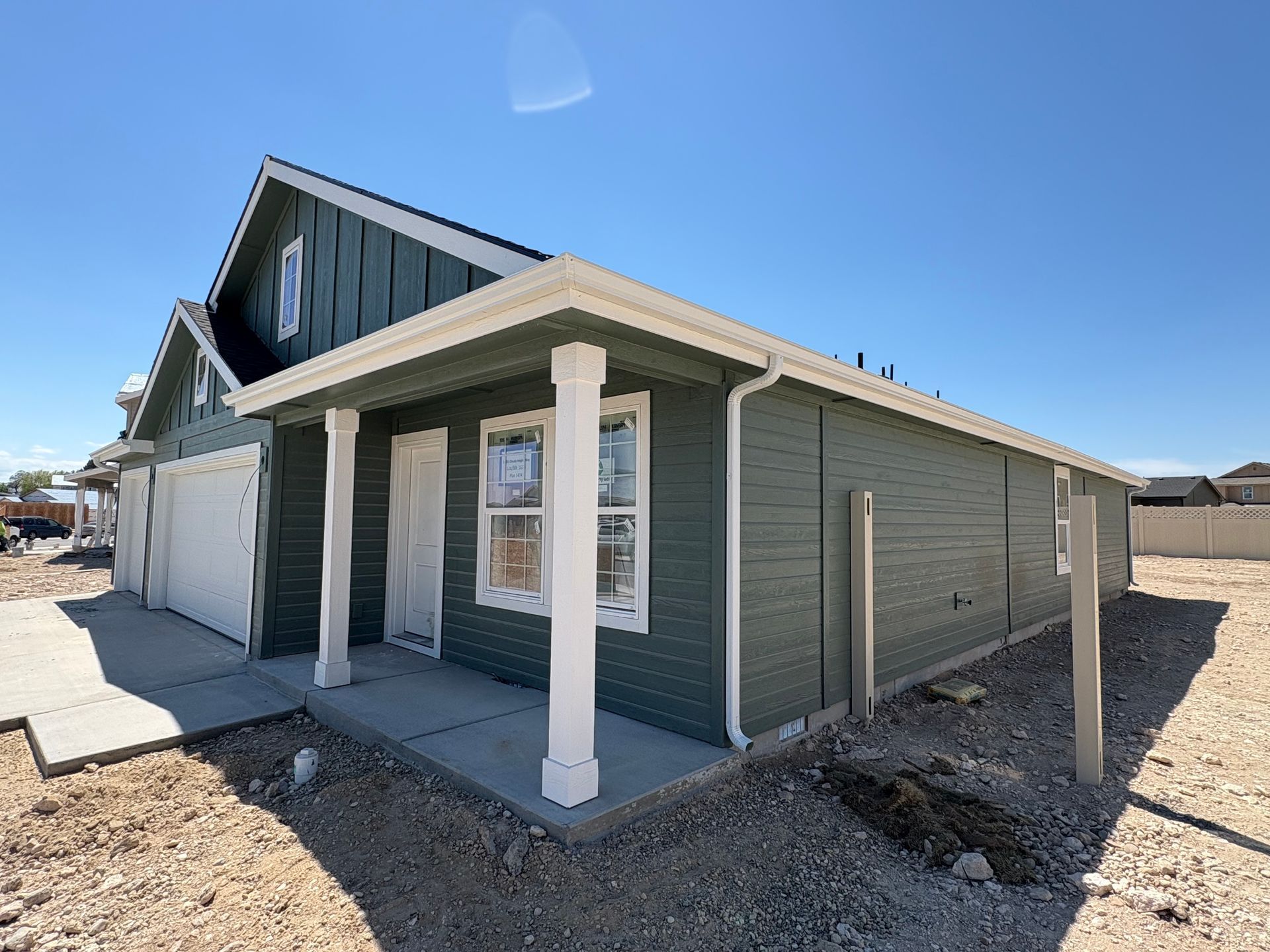 New house with green siding, white trim, and a small porch on a sunny day.