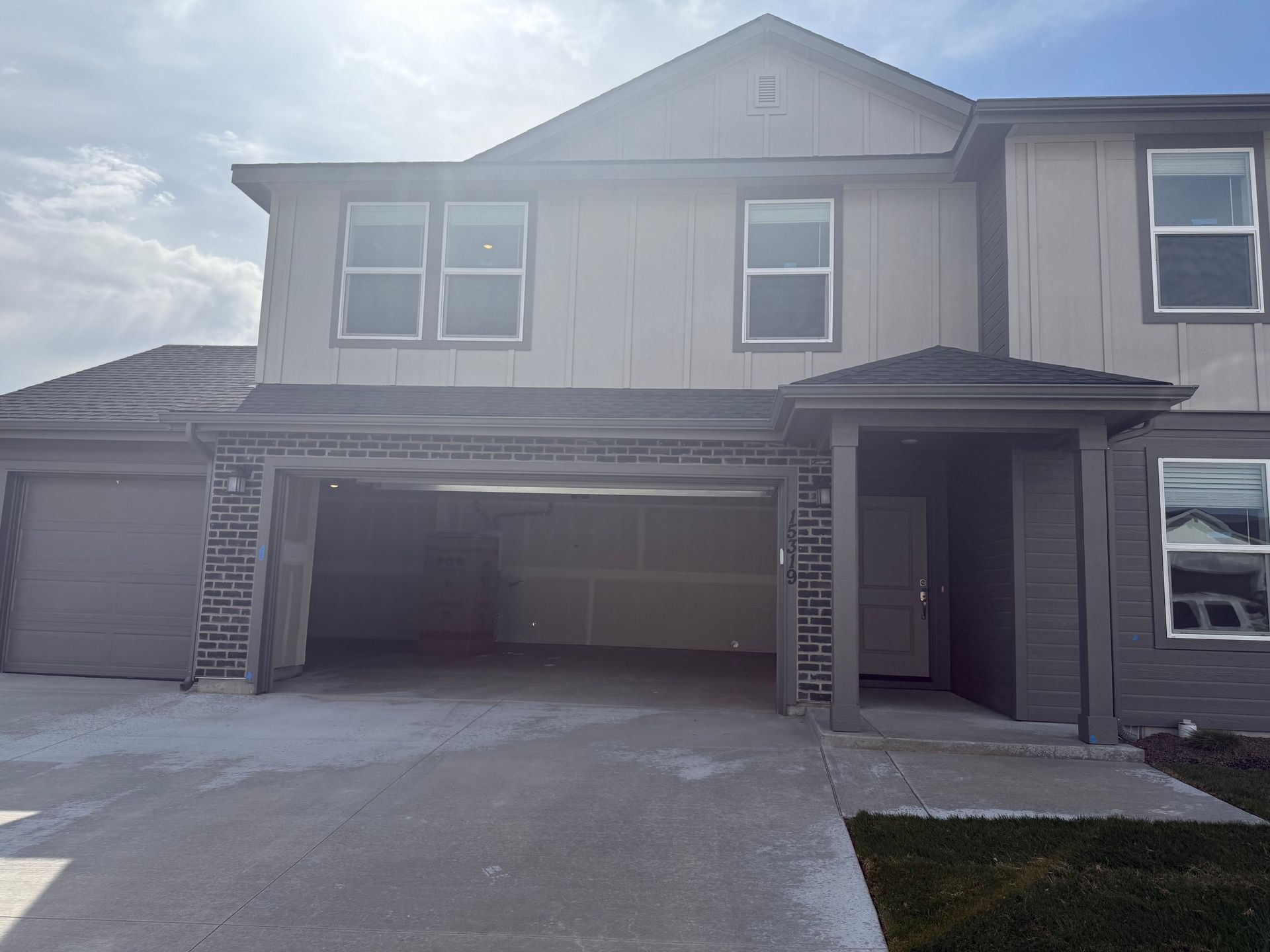 Exterior view of a two-story townhome with a garage and entrance, light gray exterior, under a cloudy sky.