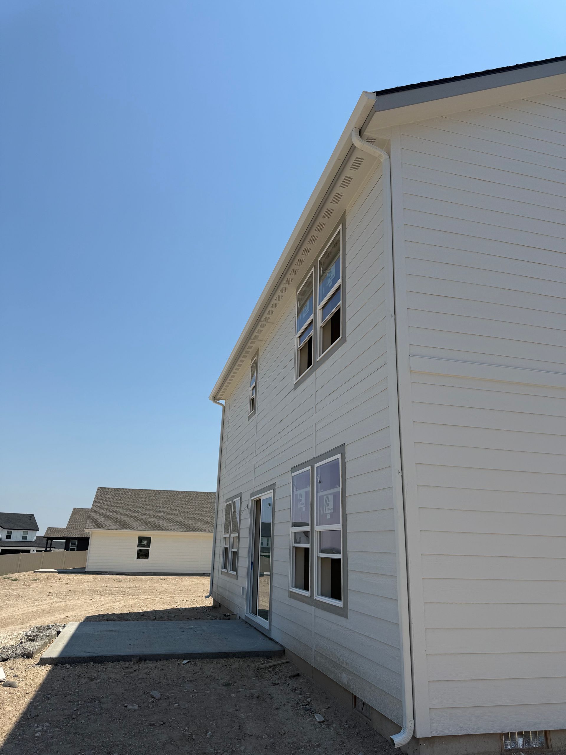 Two-story house with white siding and gray trim under a blue sky, gravel and concrete in the foreground.
