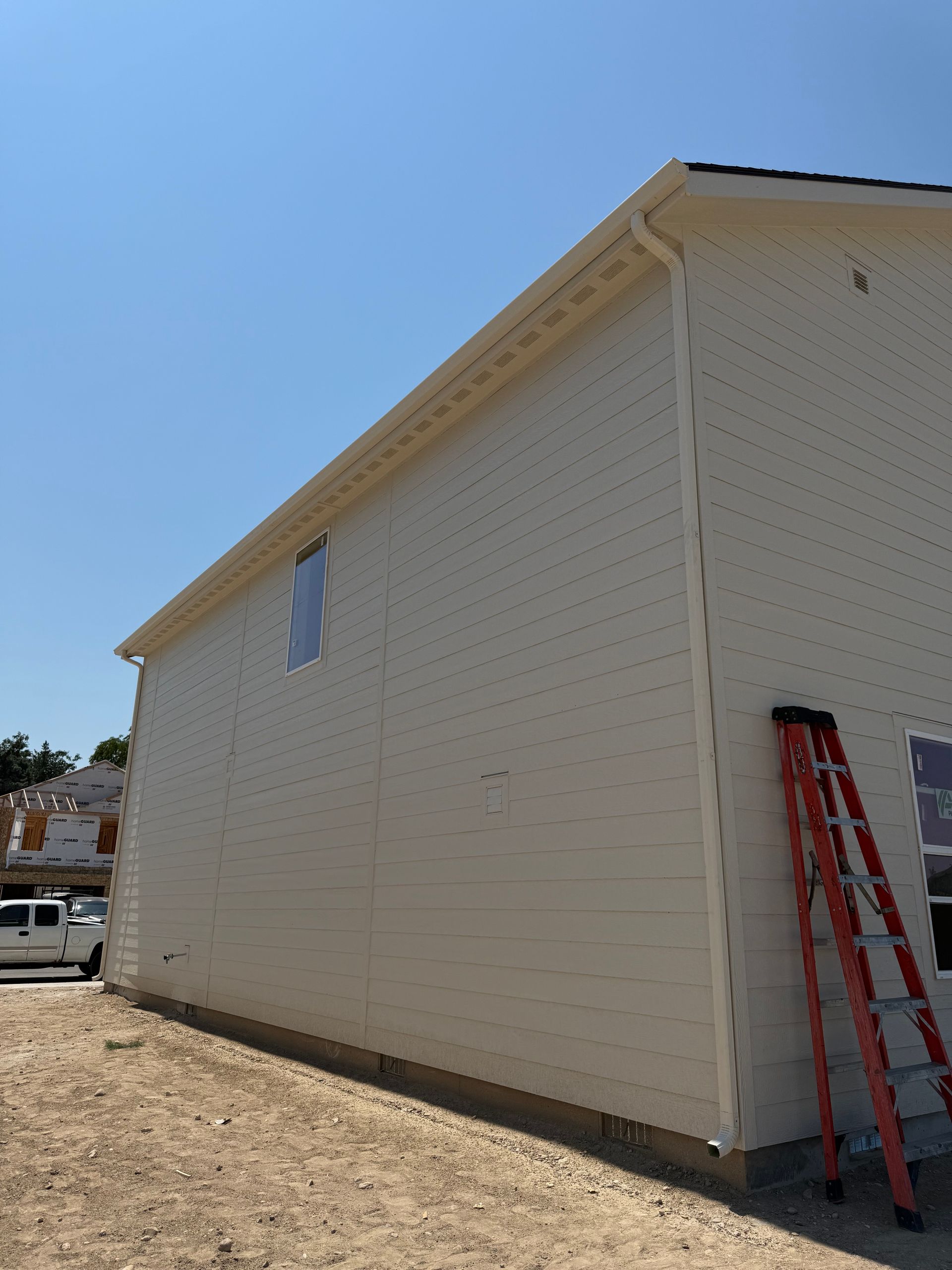 Beige siding on a two-story building under construction. An orange ladder leans against the side. Blue sky.