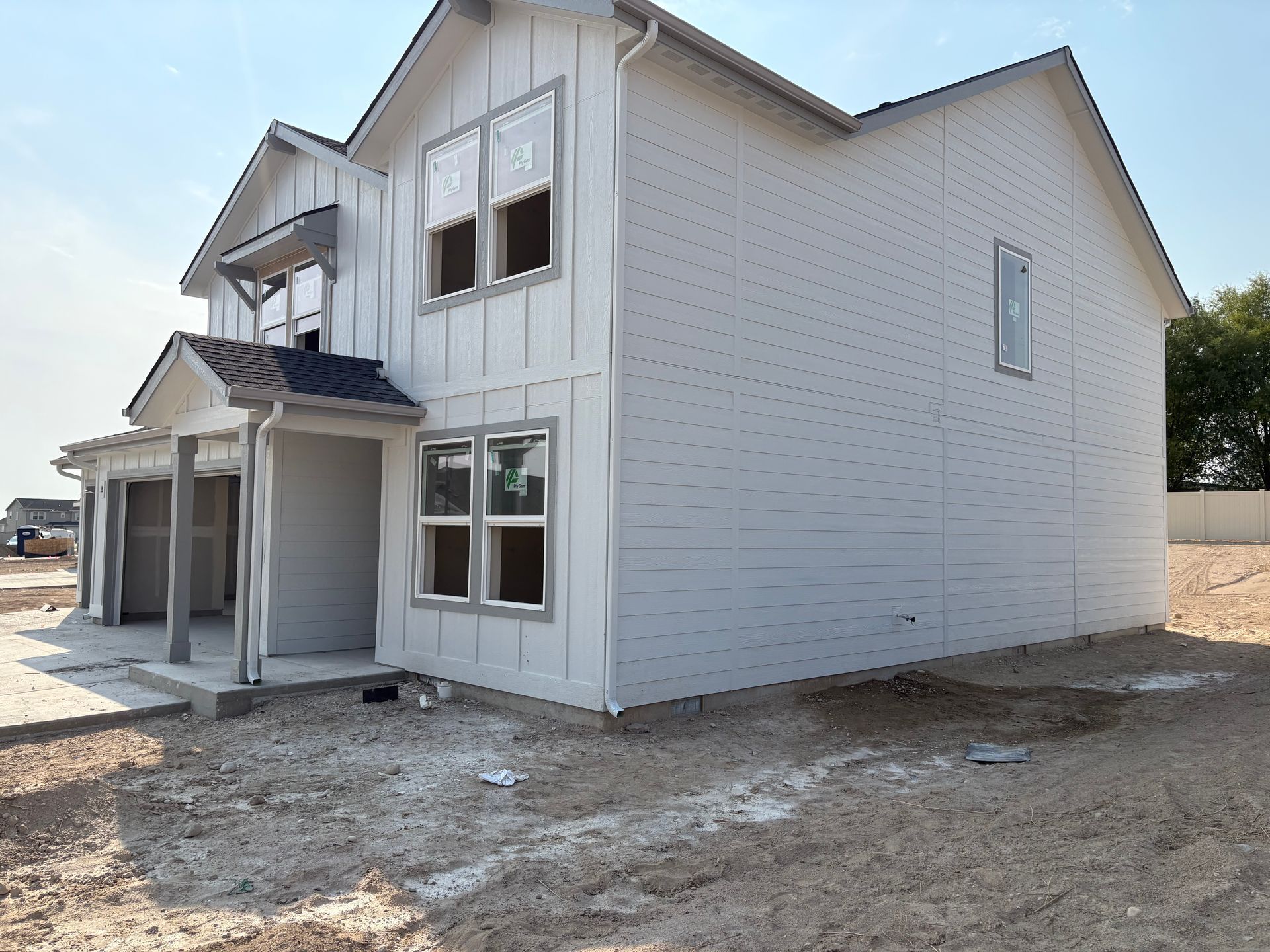 Two-story house under construction with white siding and window frames. Unfinished landscaping in the foreground.