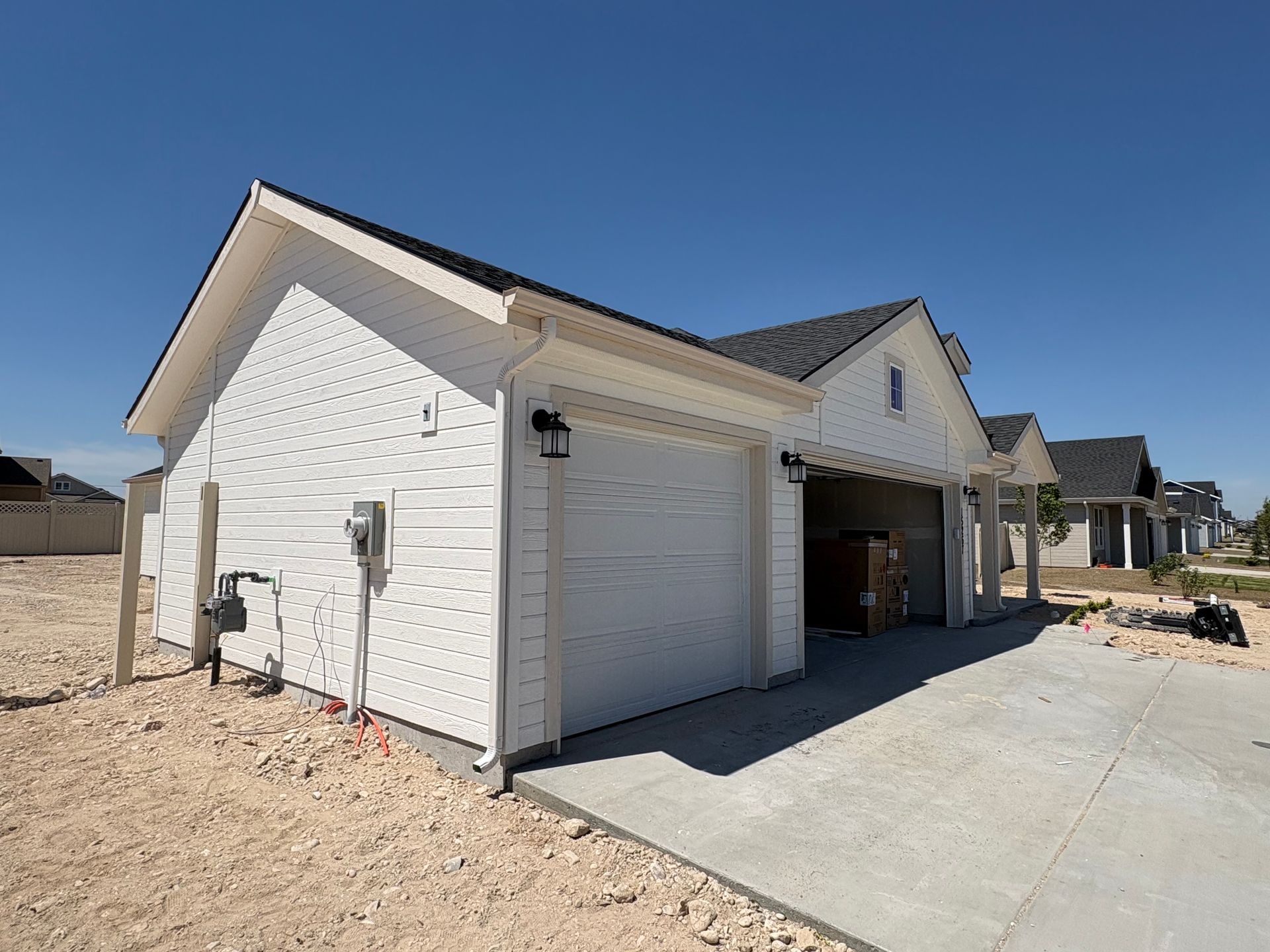 White house with two-car garage, black roof, and concrete driveway on a sunny day.