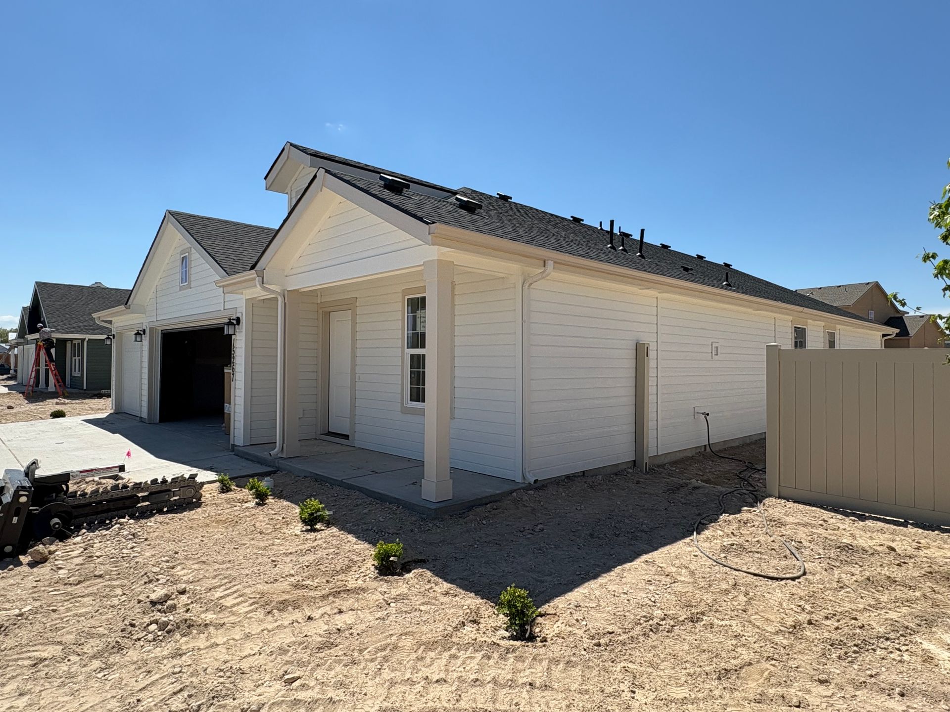 White house under construction, gravel yard, clear blue sky.